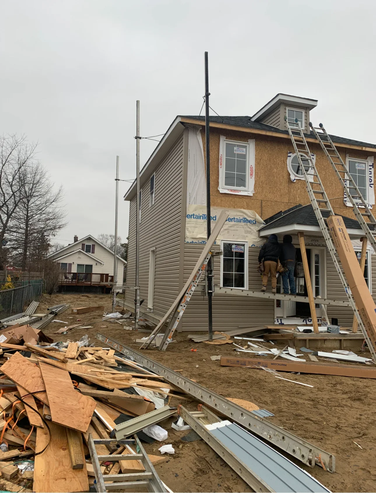 Two-story home with new vinyl siding, roof work in progress, ladders and construction materials visible