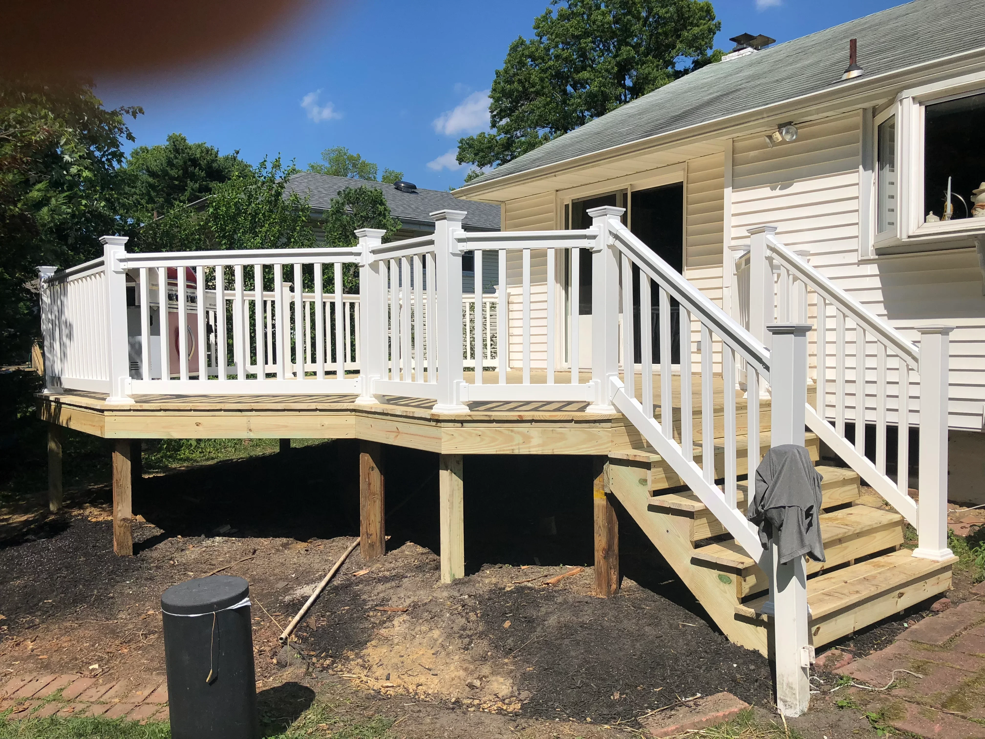 Elevated wooden deck with white vinyl railing, stairs, and black metal treads attached to house