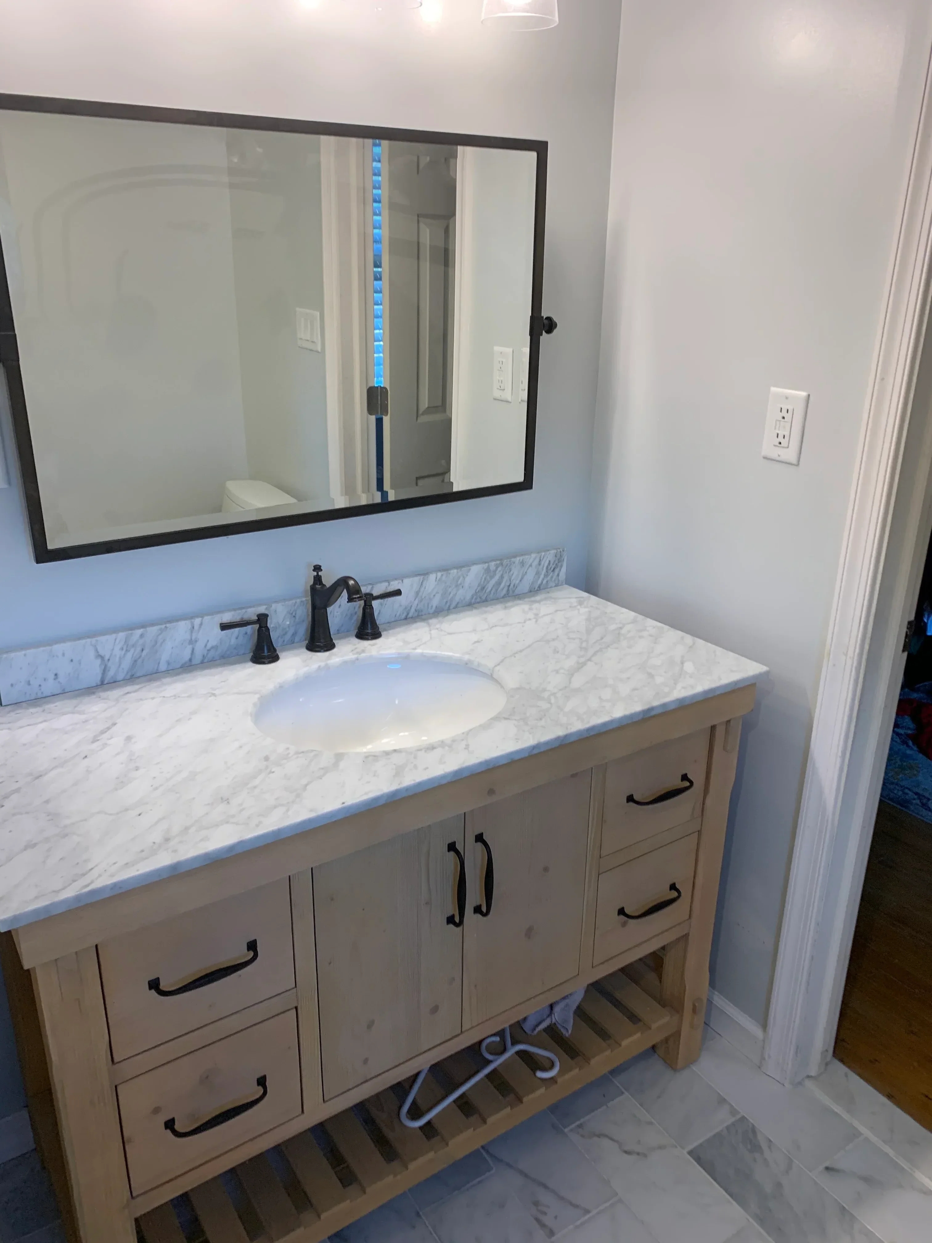 Marble vanity with wood cabinetry and frameless glass shower enclosure in bathroom