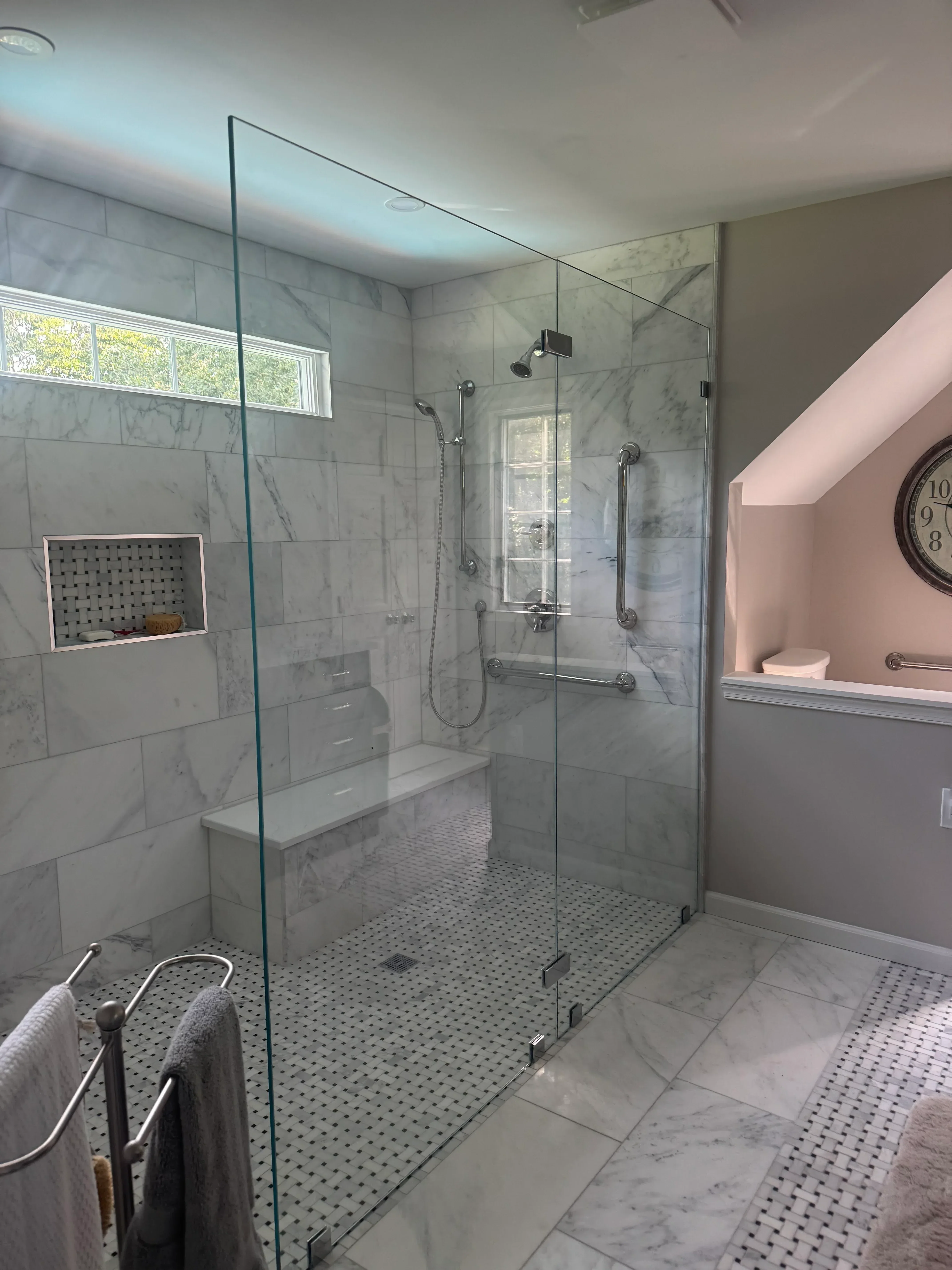 Walk-in shower with marble tile walls, penny-round mosaic floor, and frameless glass door