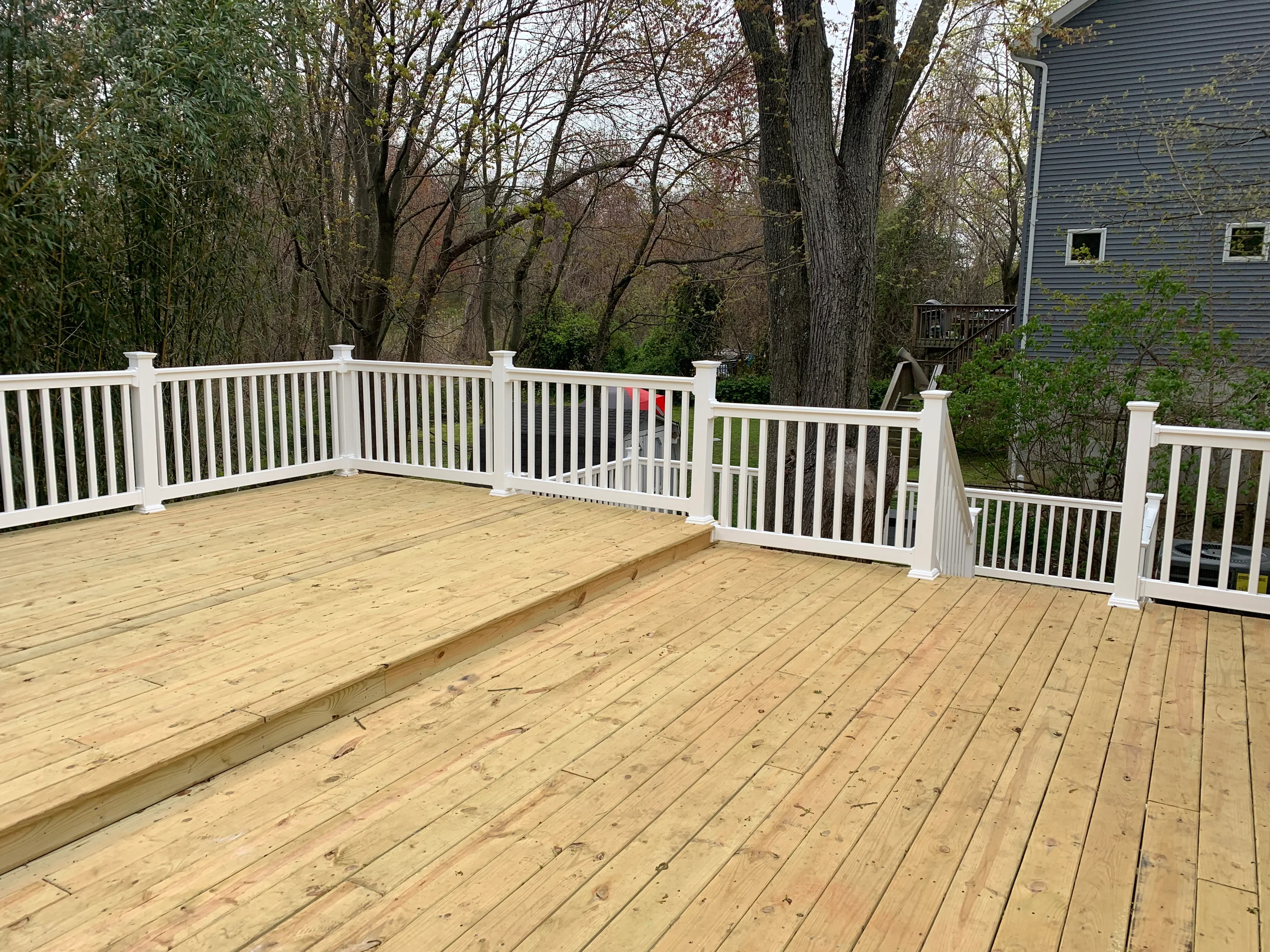 Newly constructed multi-level pressure-treated wood deck with white vinyl railing and balusters