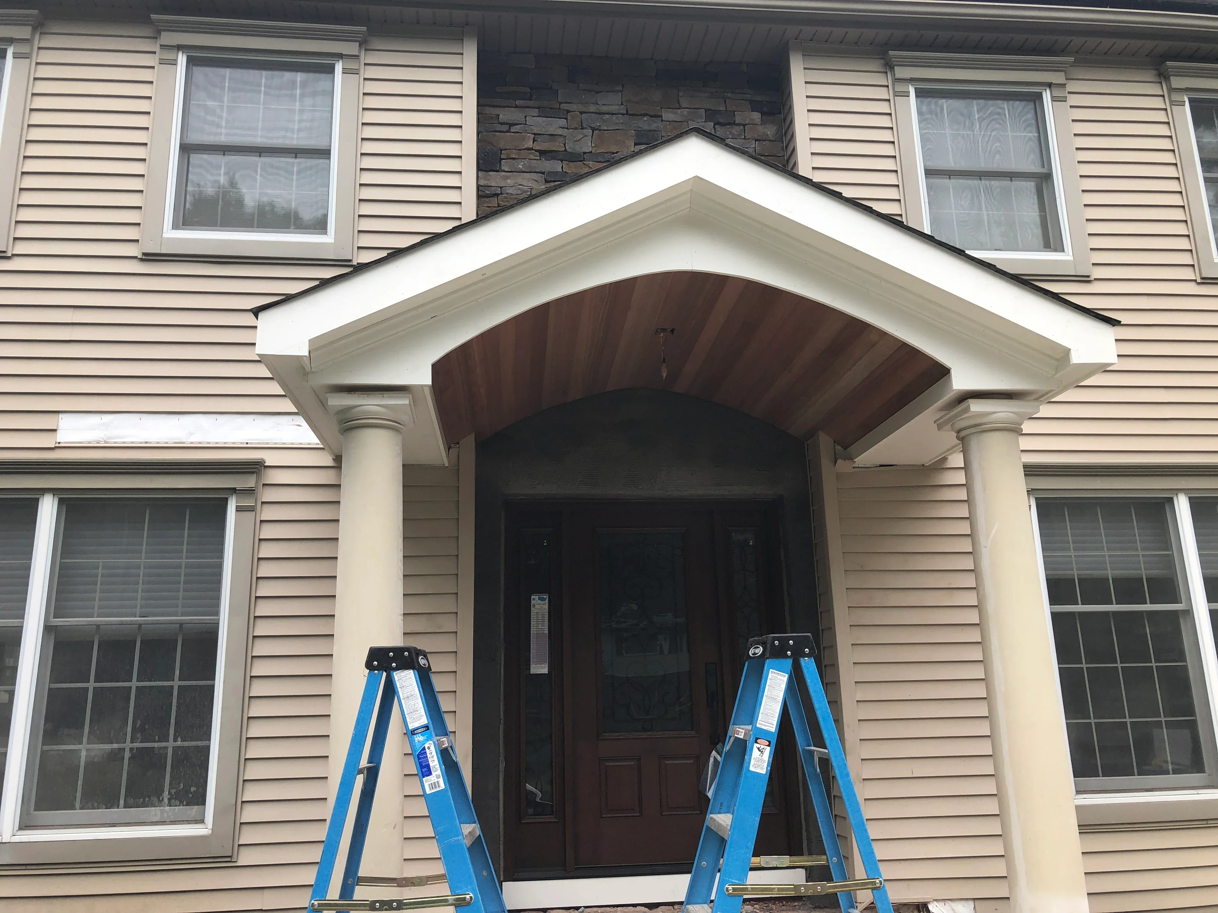 White-trimmed arched portico with dark wood soffit and columns on vinyl-sided home