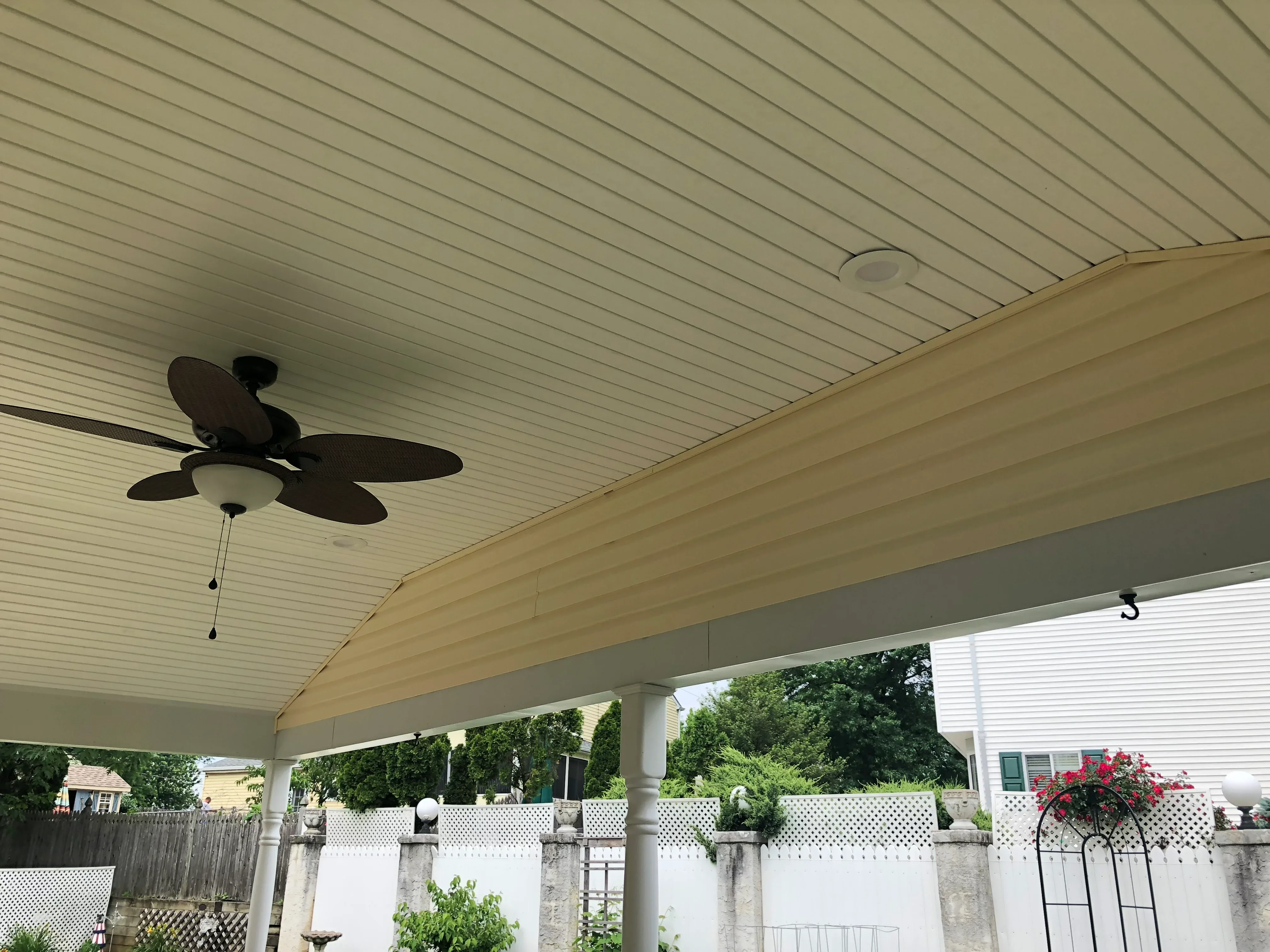 Cream metal soffit patio ceiling with black ceiling fan and recessed lighting, white vinyl railings