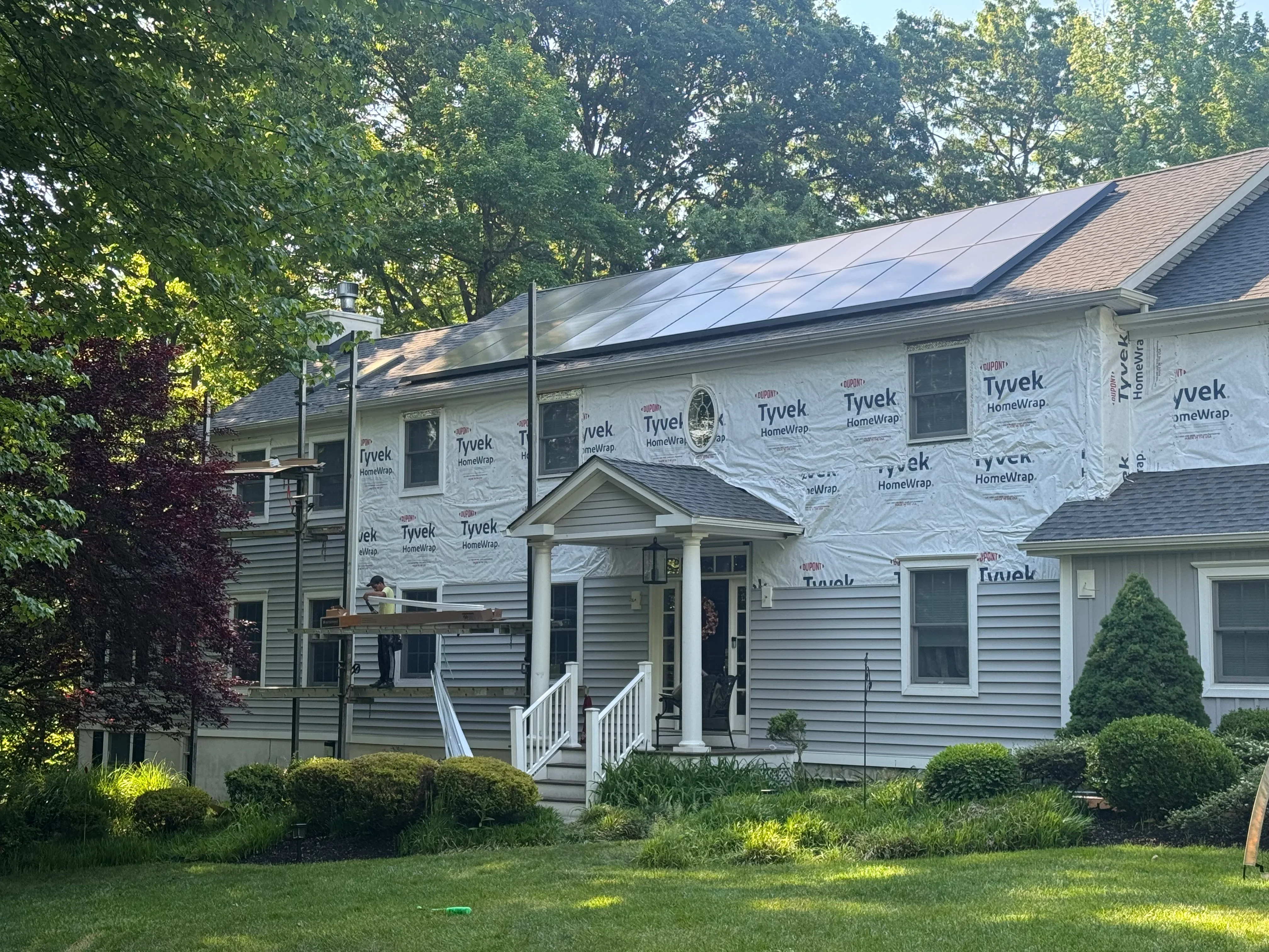 Home exterior with new solar panels, architectural shingle roof, Tyvek wrap, vinyl siding, and white entry portico