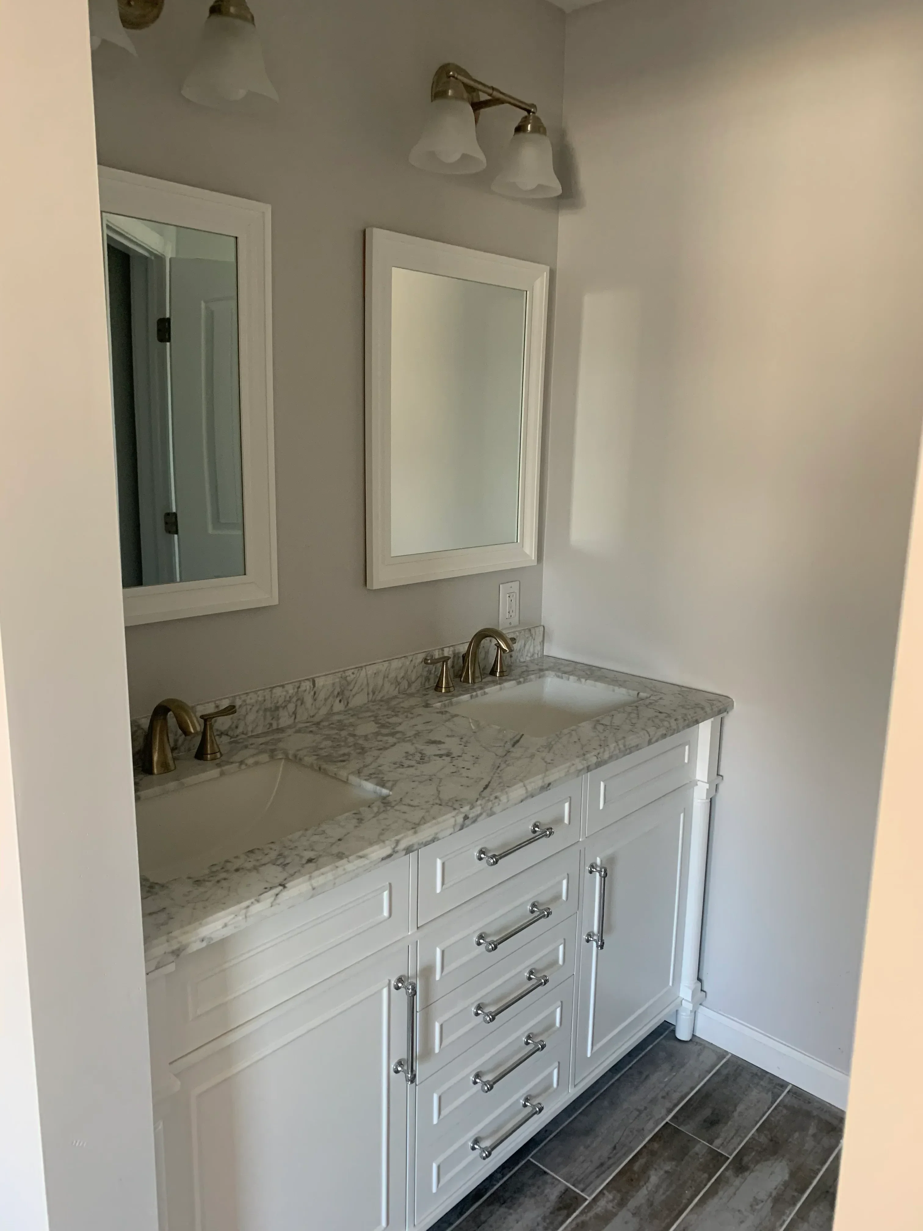 Marble countertop vanity with white cabinetry, brass hardware, and recessed medicine cabinet in bathroom