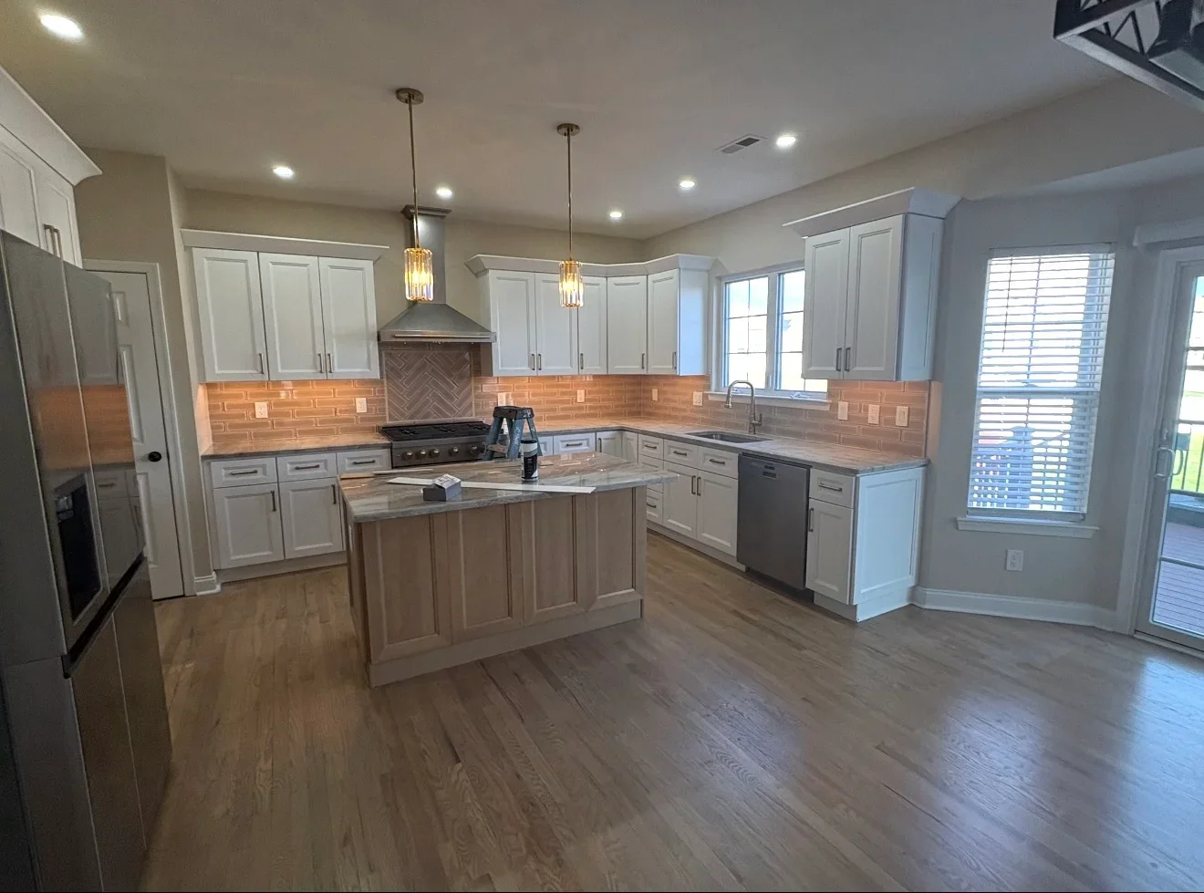 White cabinetry kitchen with herringbone brick backsplash, wood island, and stainless steel appliances