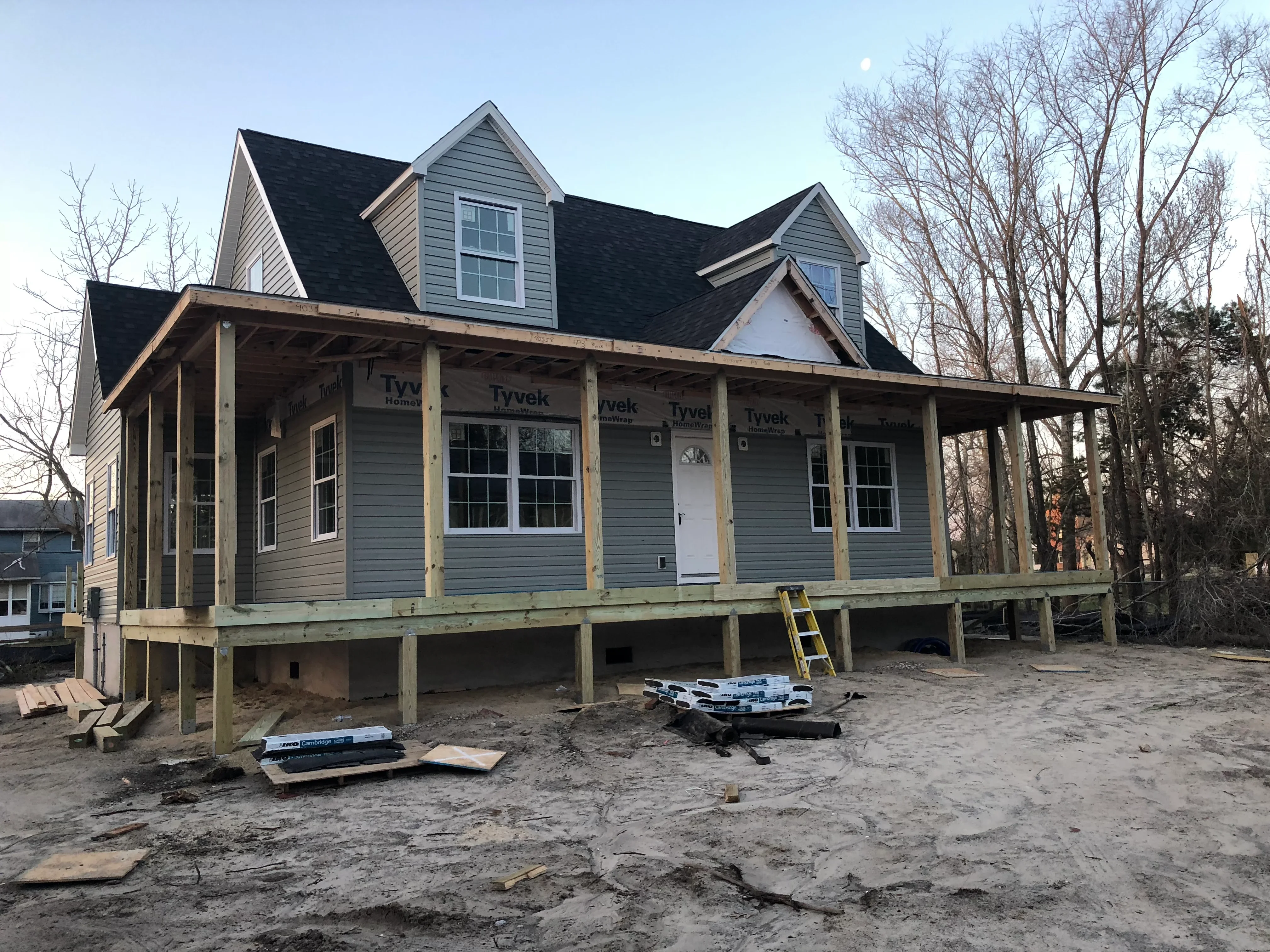 Two-story home under construction with gray siding, black roof, and wooden porch framing