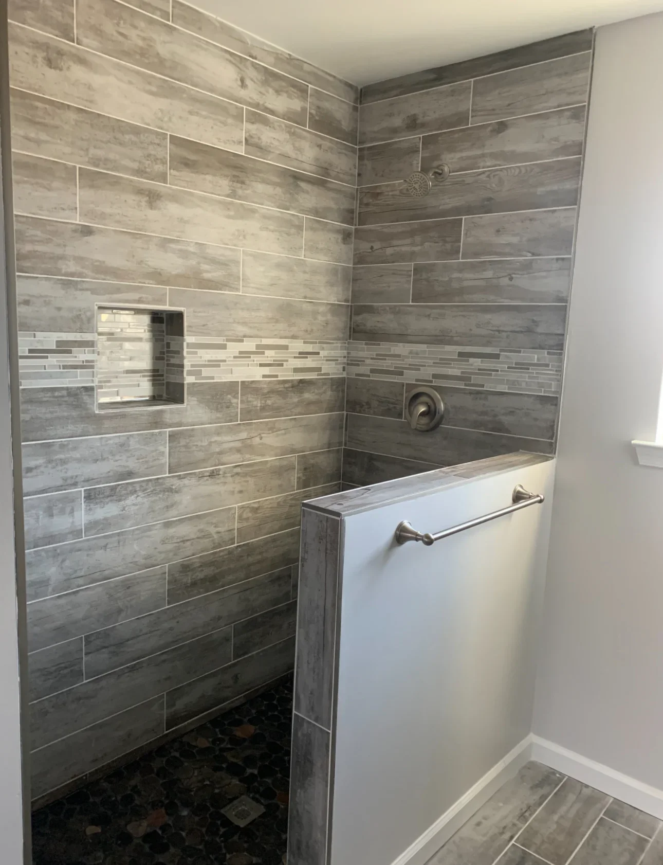 Shower with gray wood-look tile, glass mosaic accent strip, and frameless glass enclosure