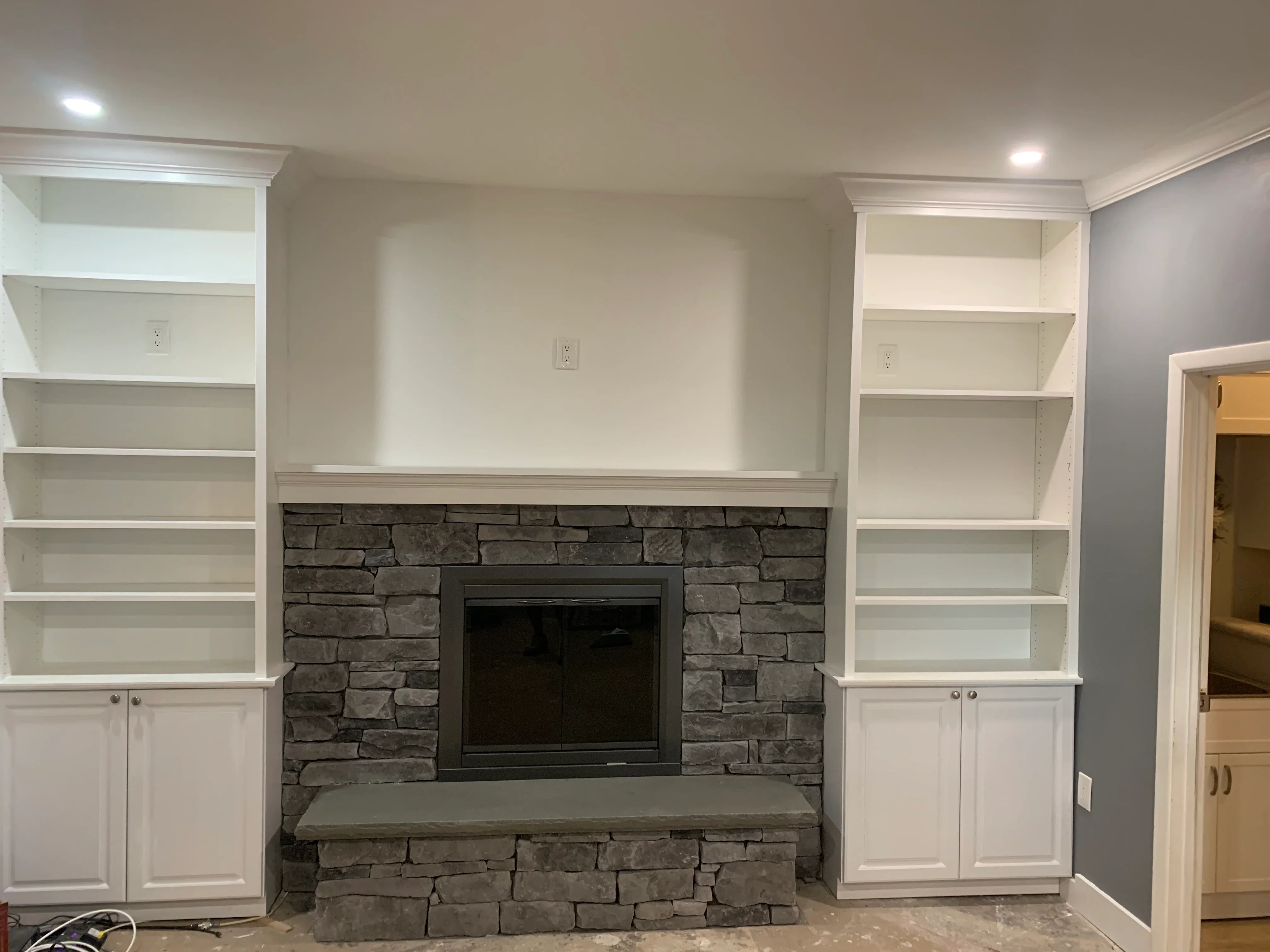 White built-in shelving with lower cabinets flanking dark stacked stone fireplace with TV niche