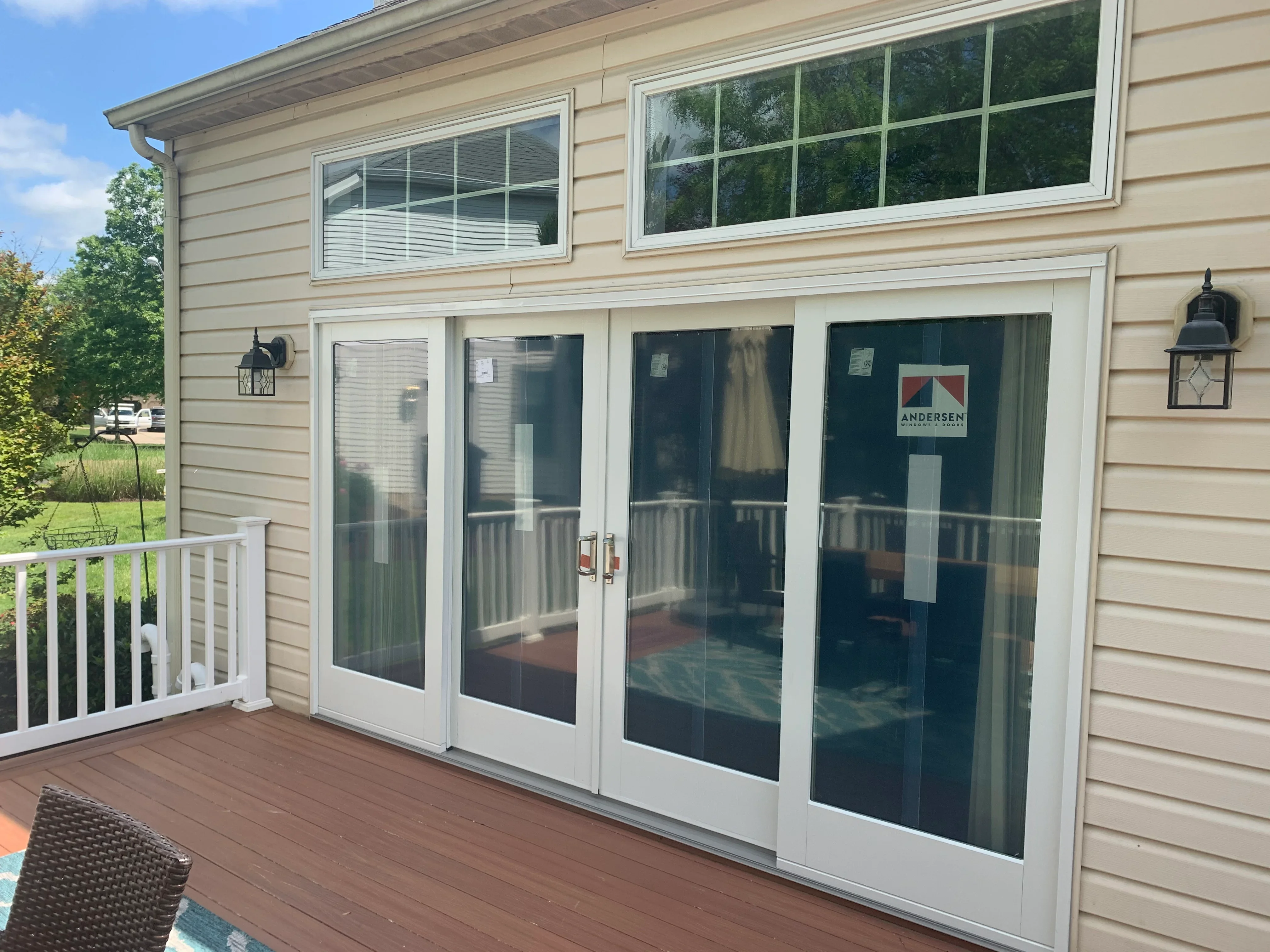 Four white-framed patio doors with dark glass installed on tan siding above composite deck