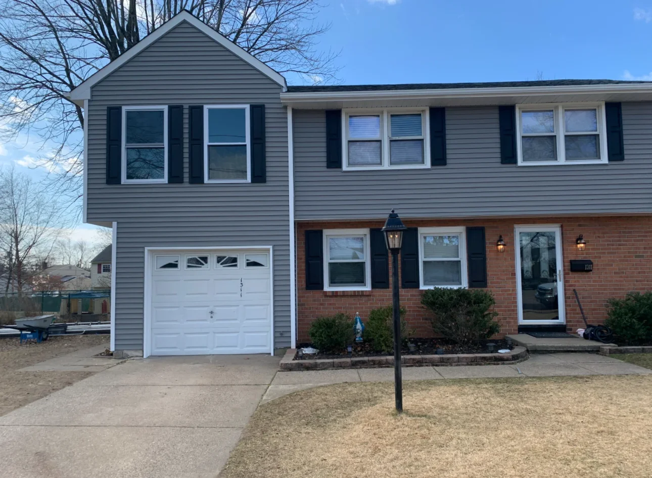 Split-level home with gray vinyl siding, white garage door, brick veneer, replacement windows, and black shutters