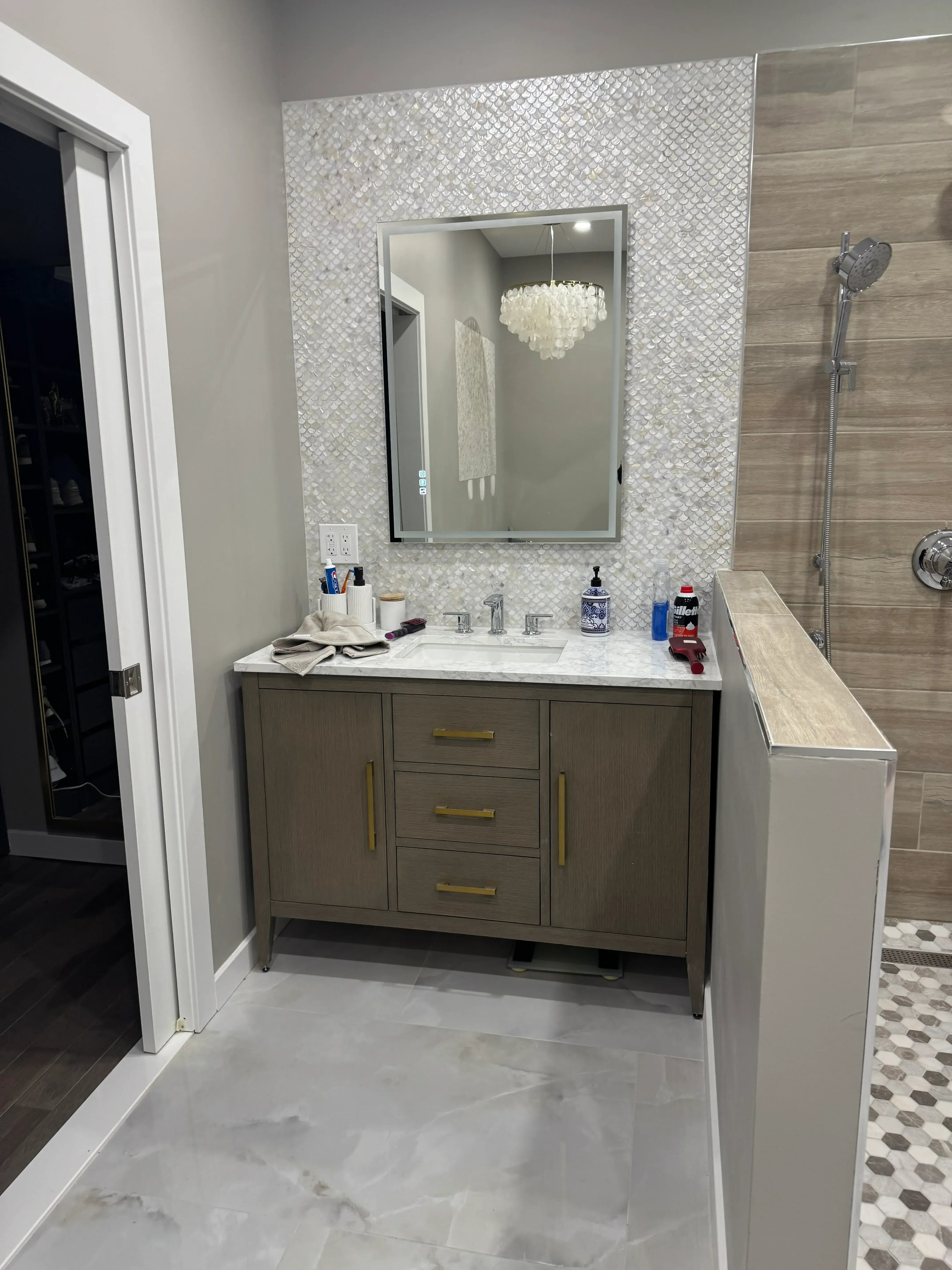 Frameless glass shower with marble mosaic tile surround and chrome fixtures in renovated bathroom