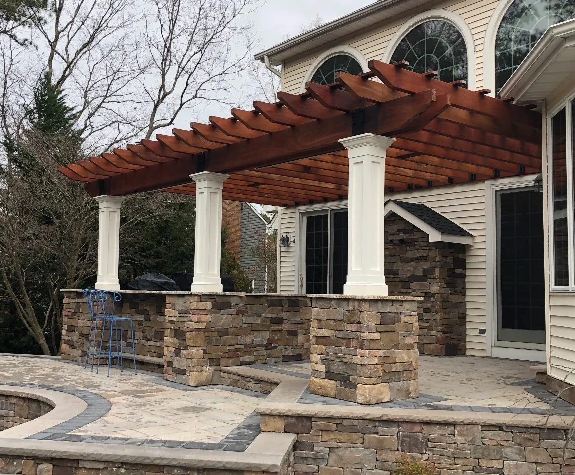 Cedar pergola with white columns over stone veneer patio and walls