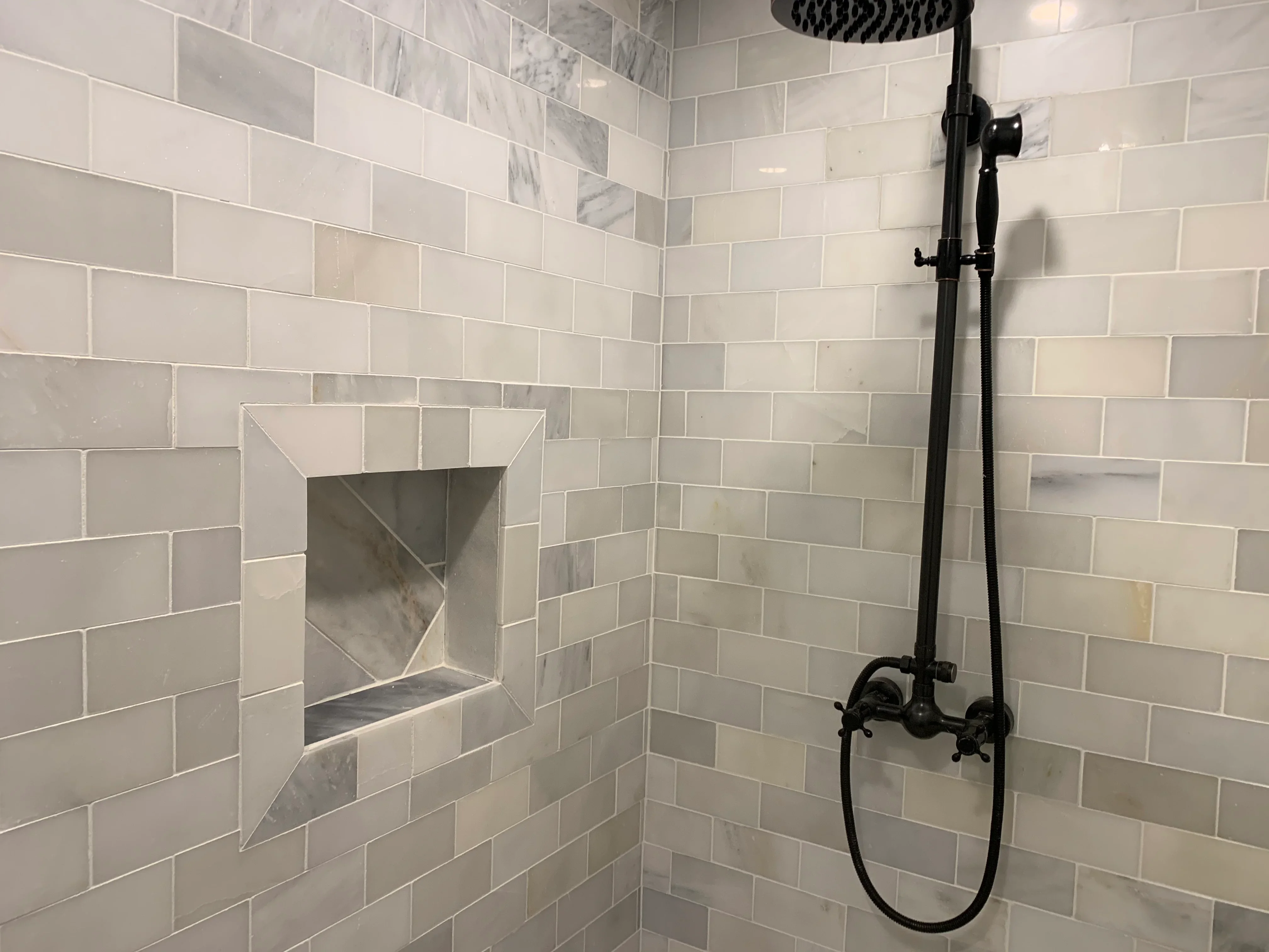Subway tile shower with marble niche and black fixtures