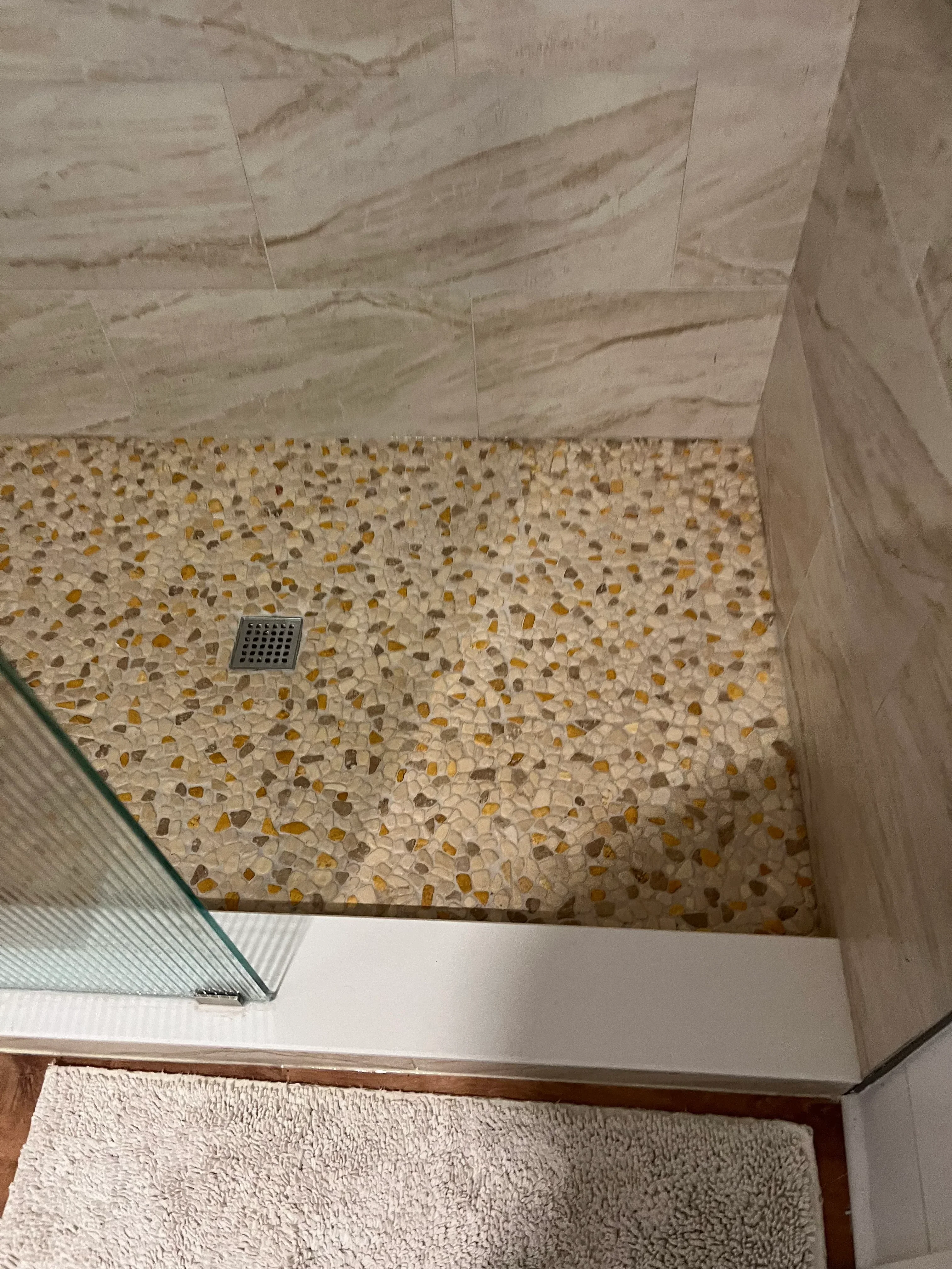 Shower interior with pebble mosaic accent wall and marble-look tile surround