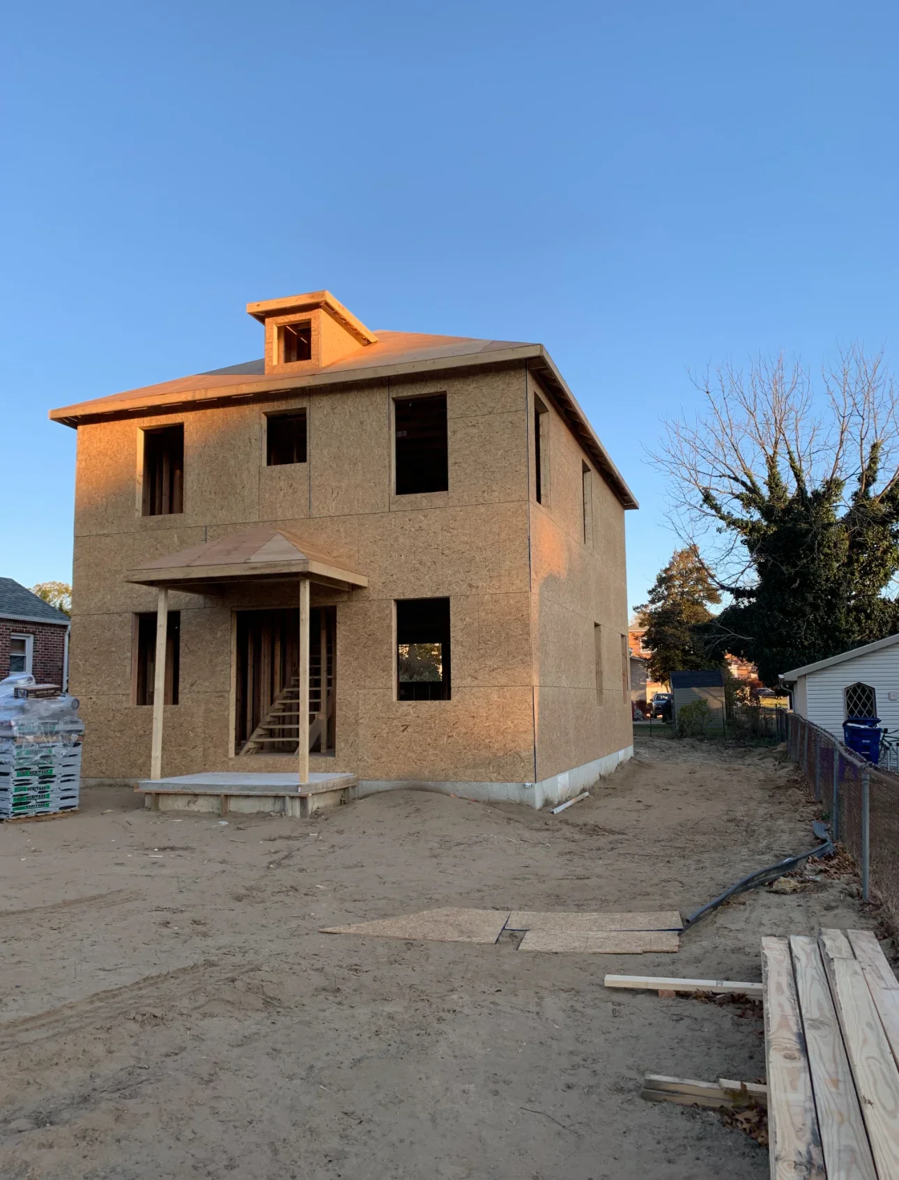 Two-story house frame with OSB sheathing, wooden porch posts, and open window openings under construction