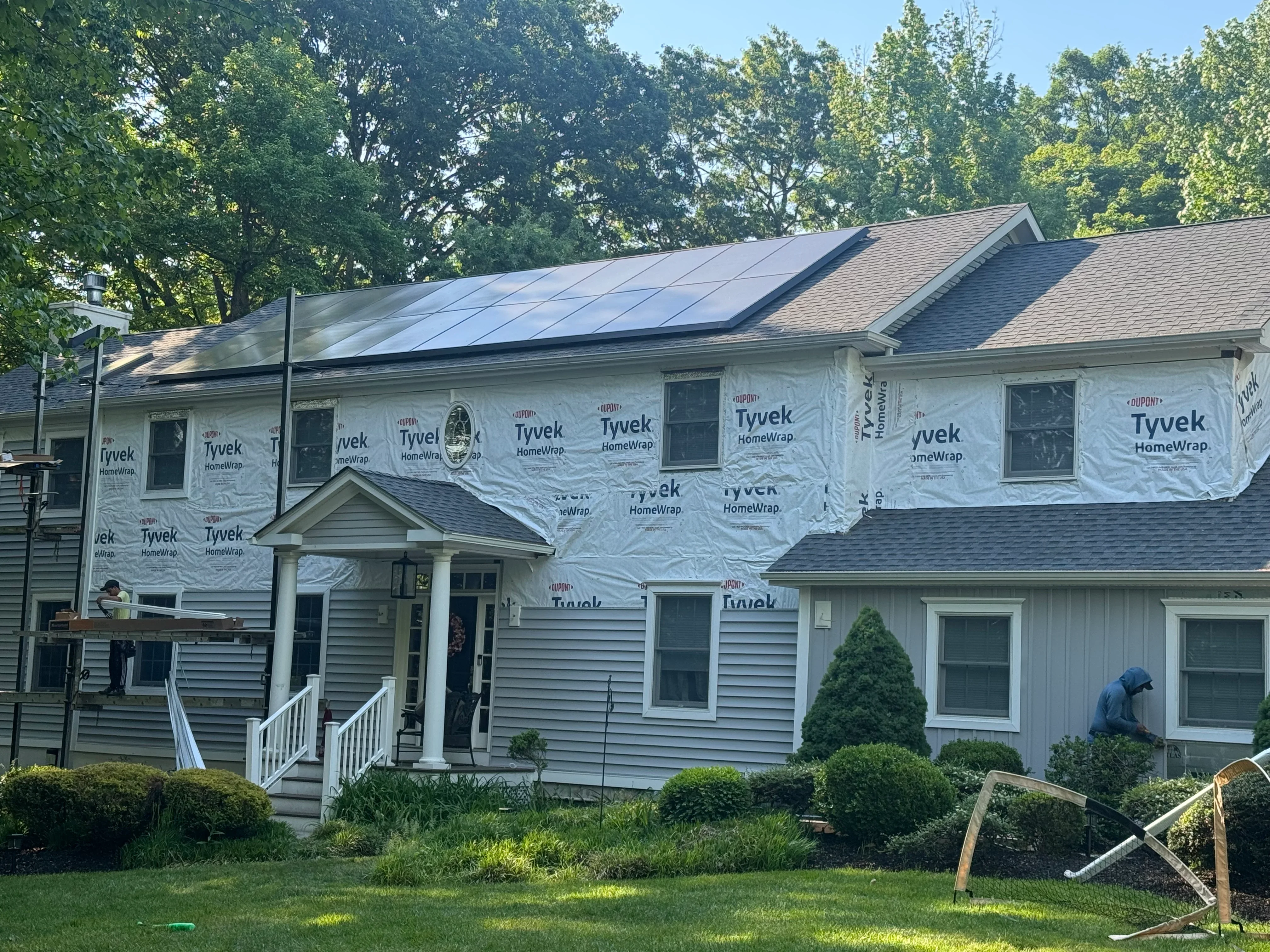 Two-story home with new asphalt shingle roof, Tyvek HomeWrap, vinyl siding, and new windows during renovation
