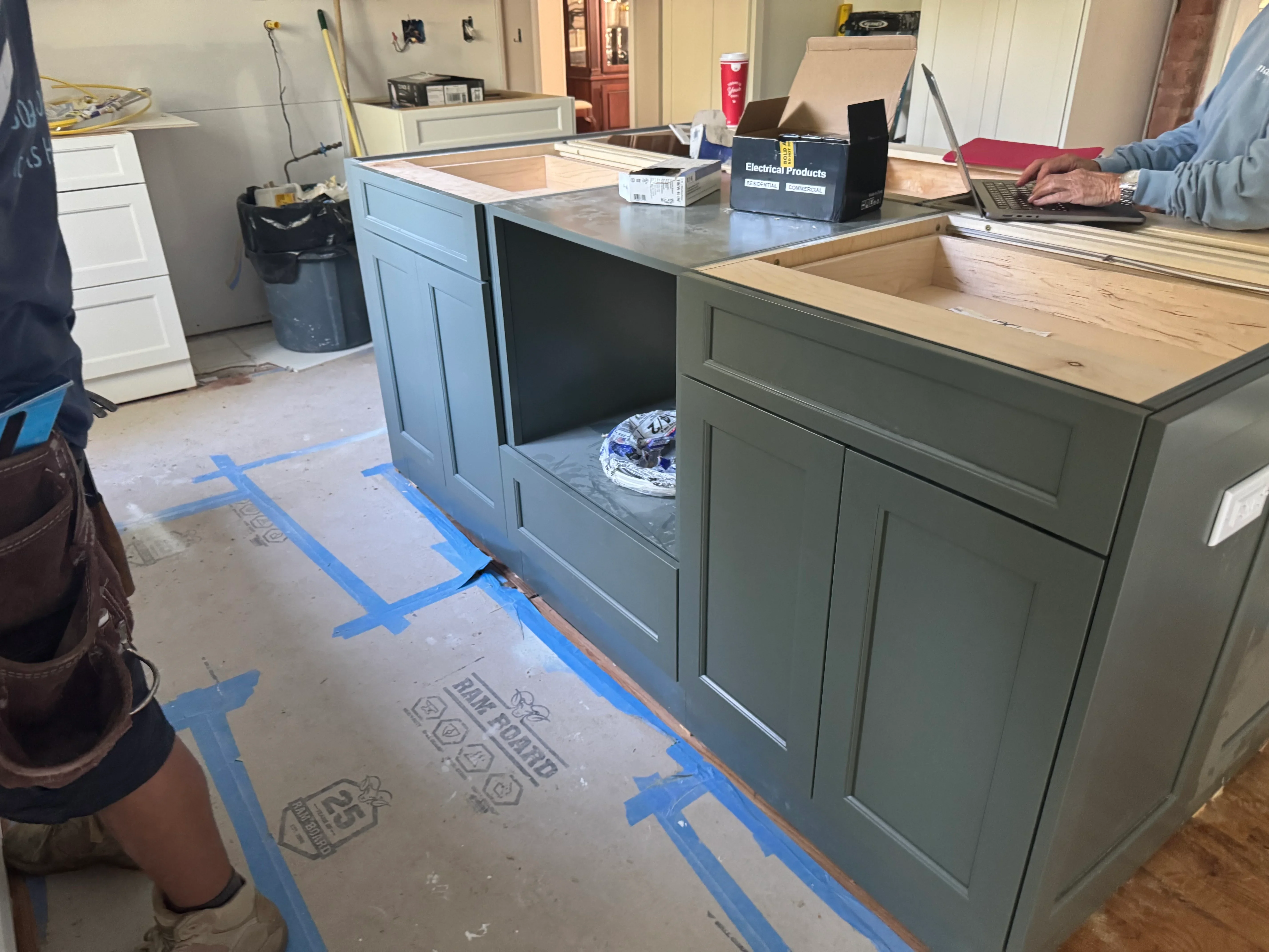 Kitchen remodel in progress with painted blue and green cabinetry, new countertops, and protective floor masking