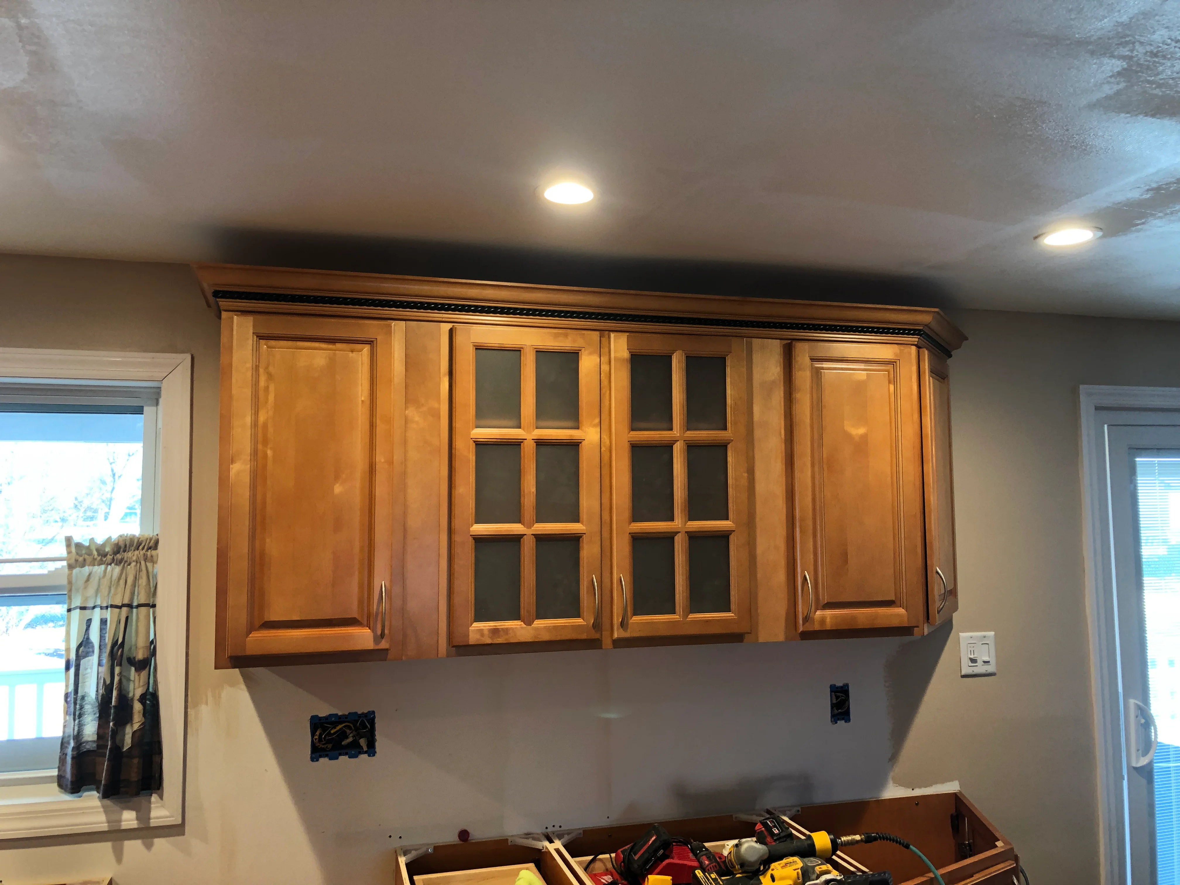 Cherry wood wall cabinets with glass doors and recessed lighting in drywall soffit