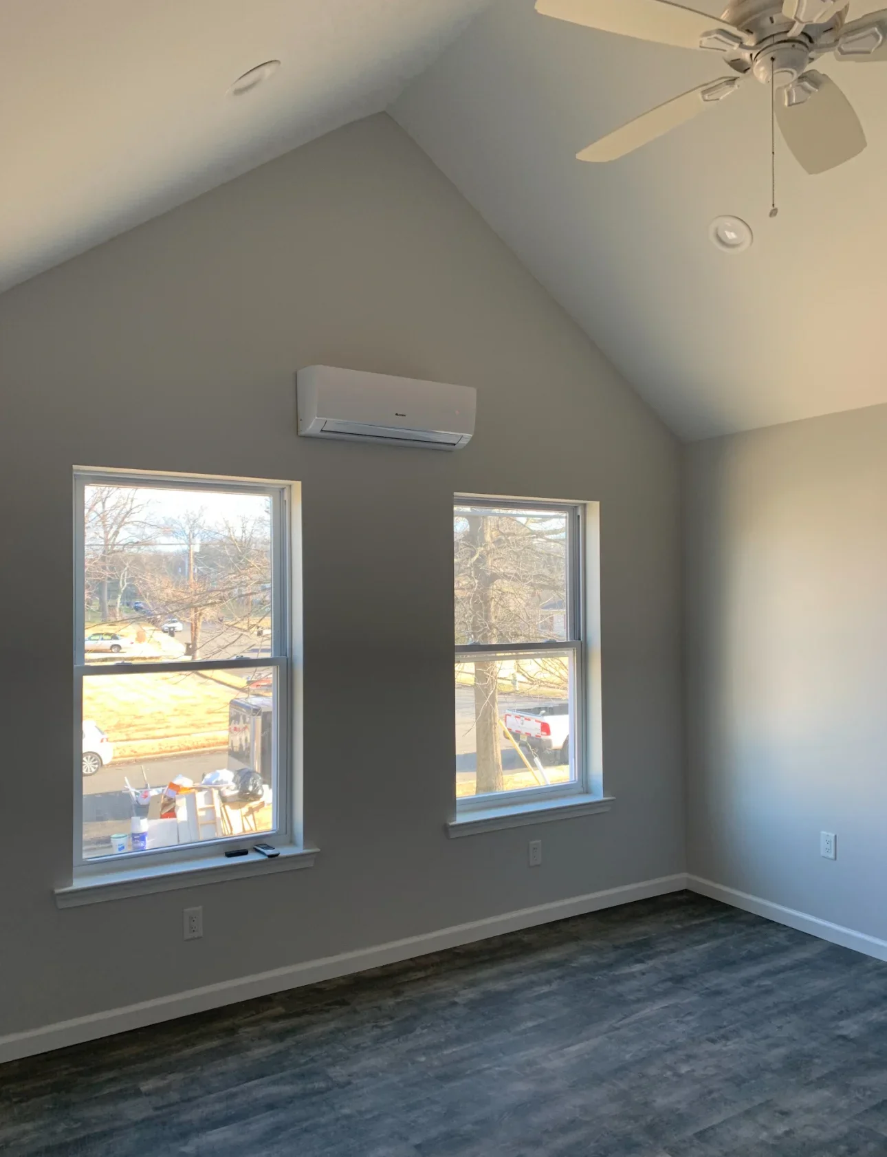 Finished attic room with vaulted drywall ceiling, two windows with trim, mini-split AC unit, recessed lights, and gray paint