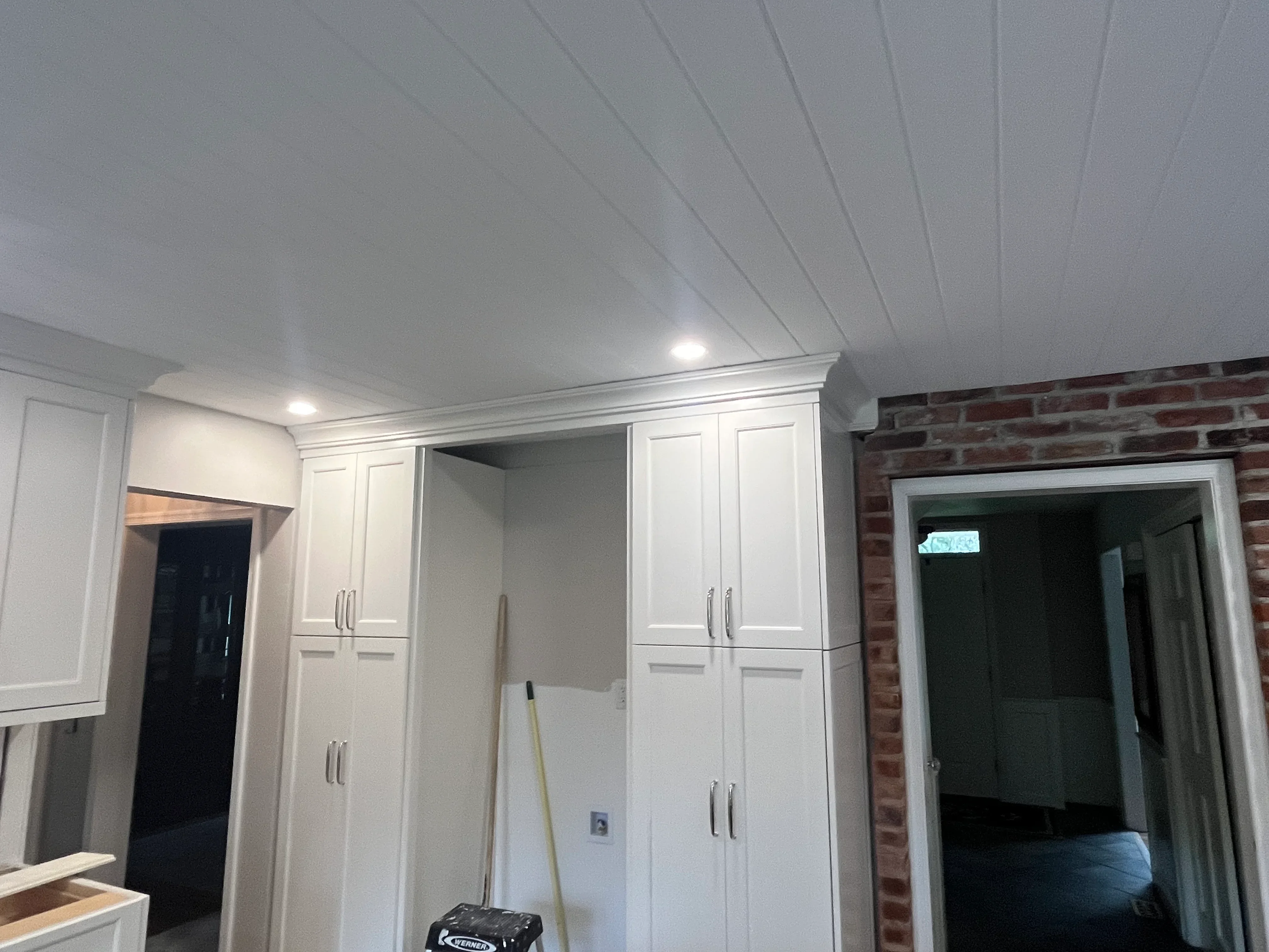 Finished basement with white cabinetry, recessed lighting, and exposed brick wall