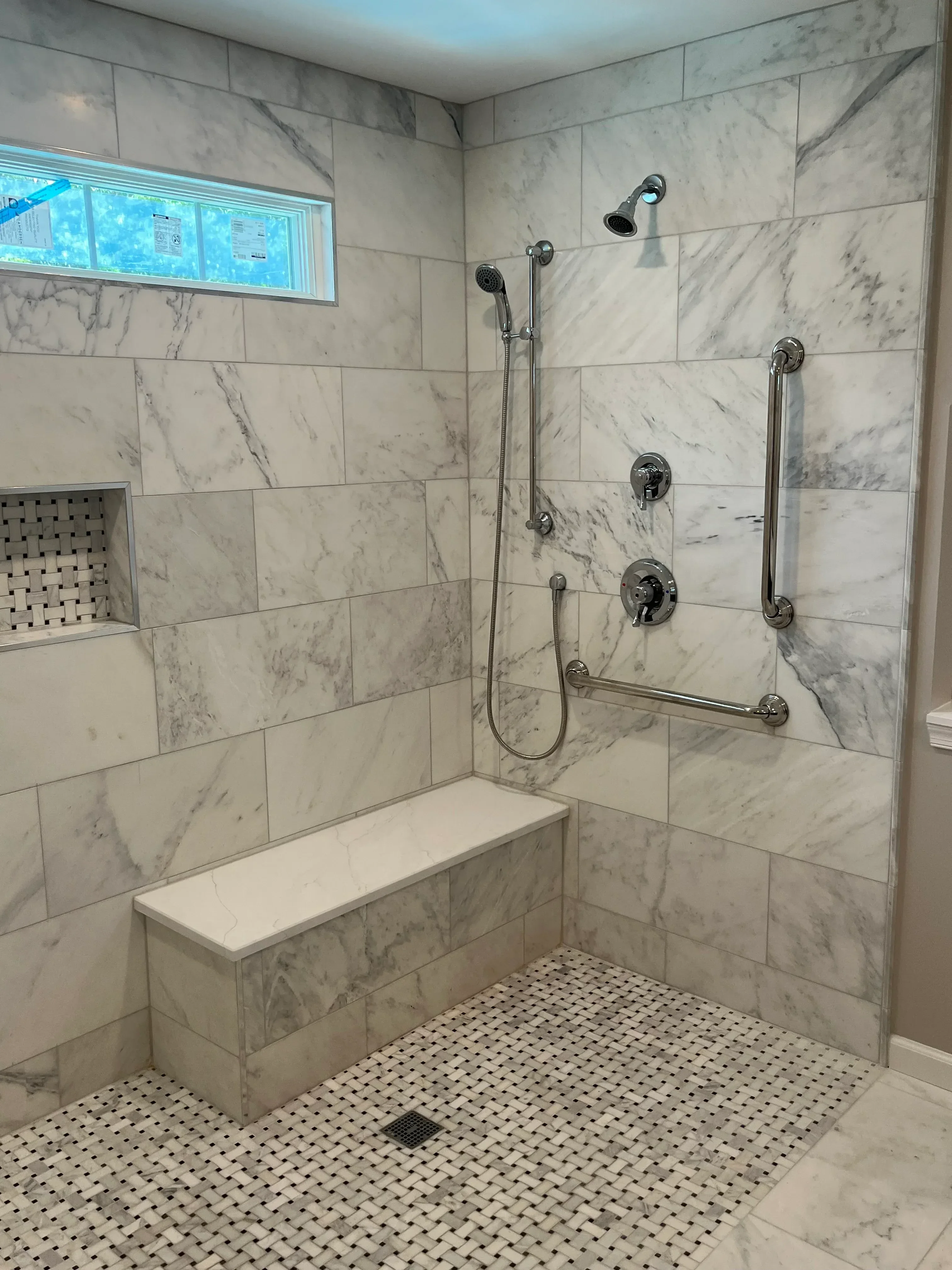 Marble tile shower with chrome fixtures, grab bars, and mosaic accent wall