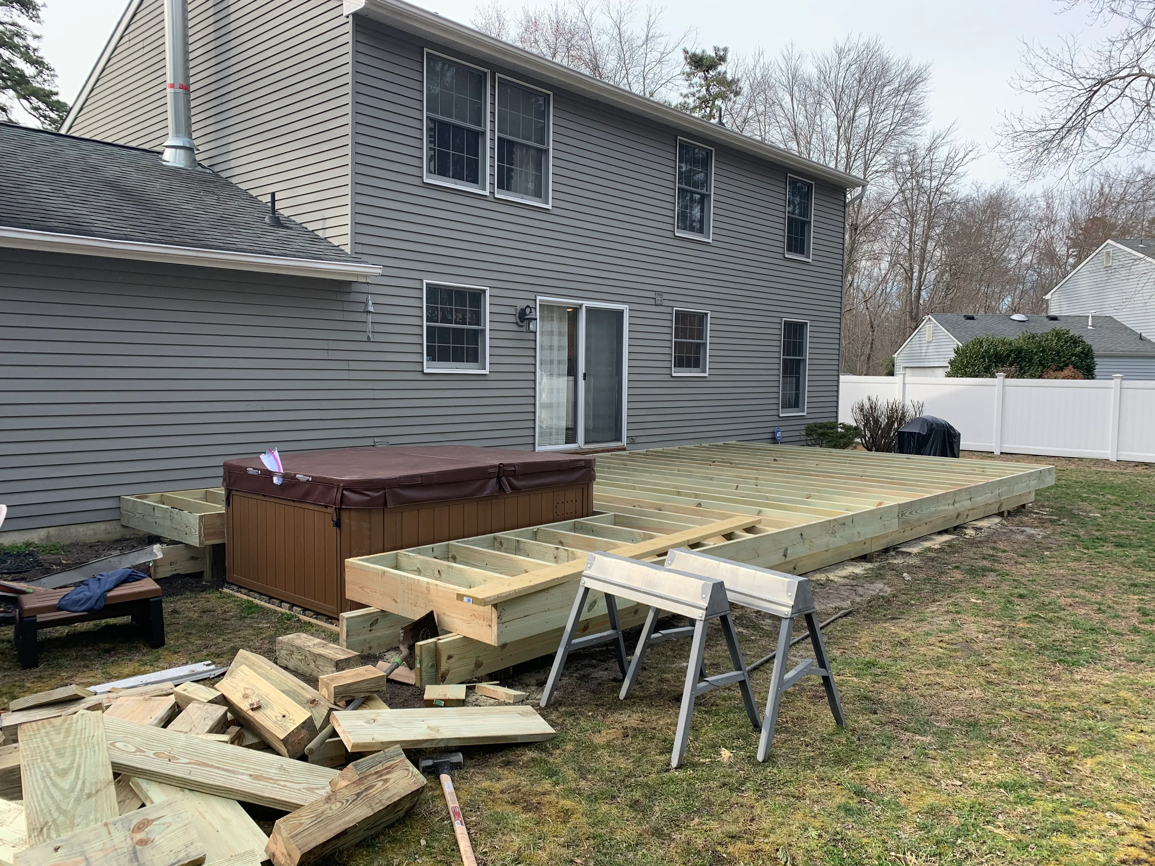 Pressure-treated wood deck framing with joists and beams under construction next to residential home
