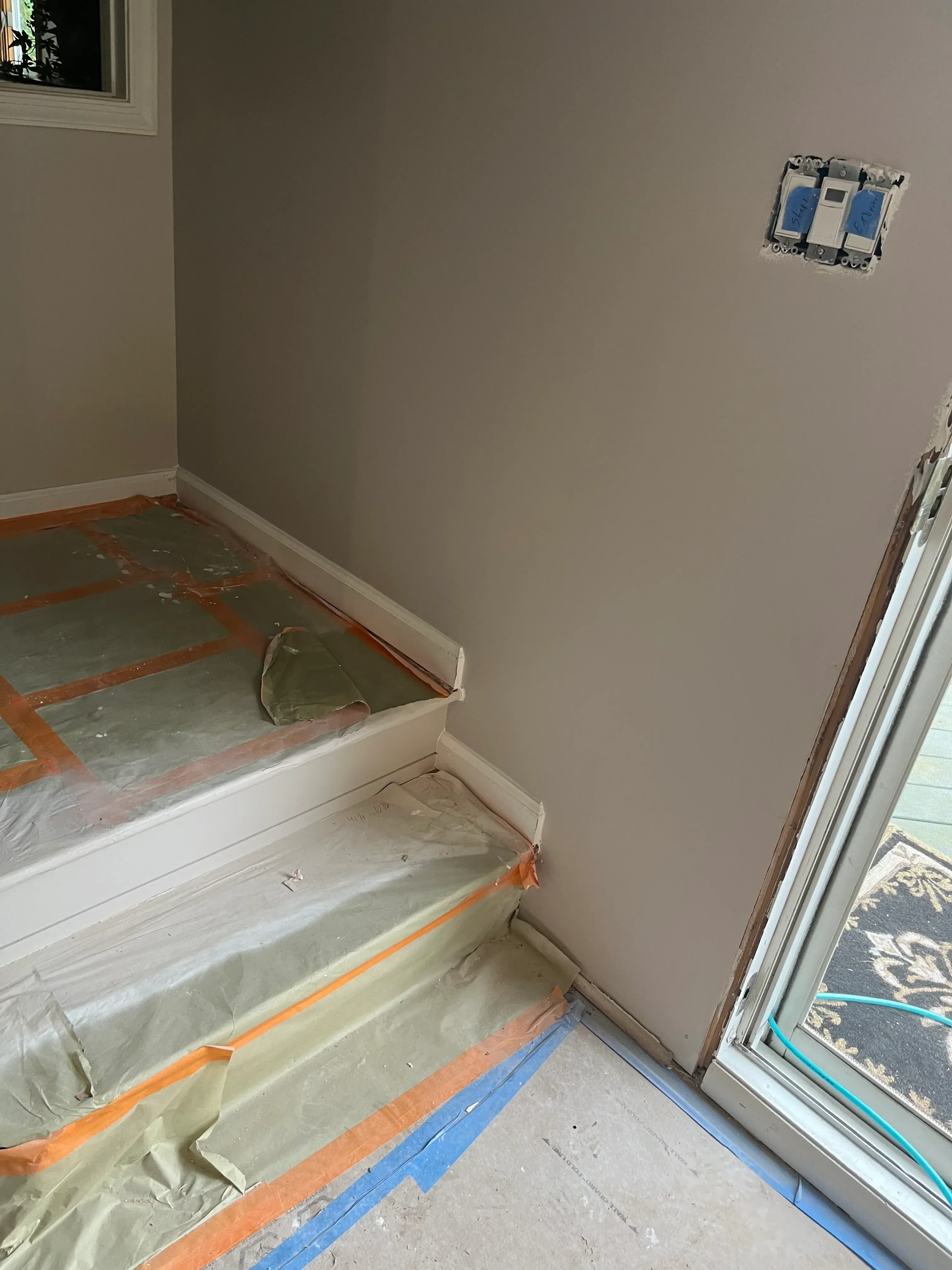 Drywall installation with electrical boxes, protective sheeting, and painter's tape on interior walls
