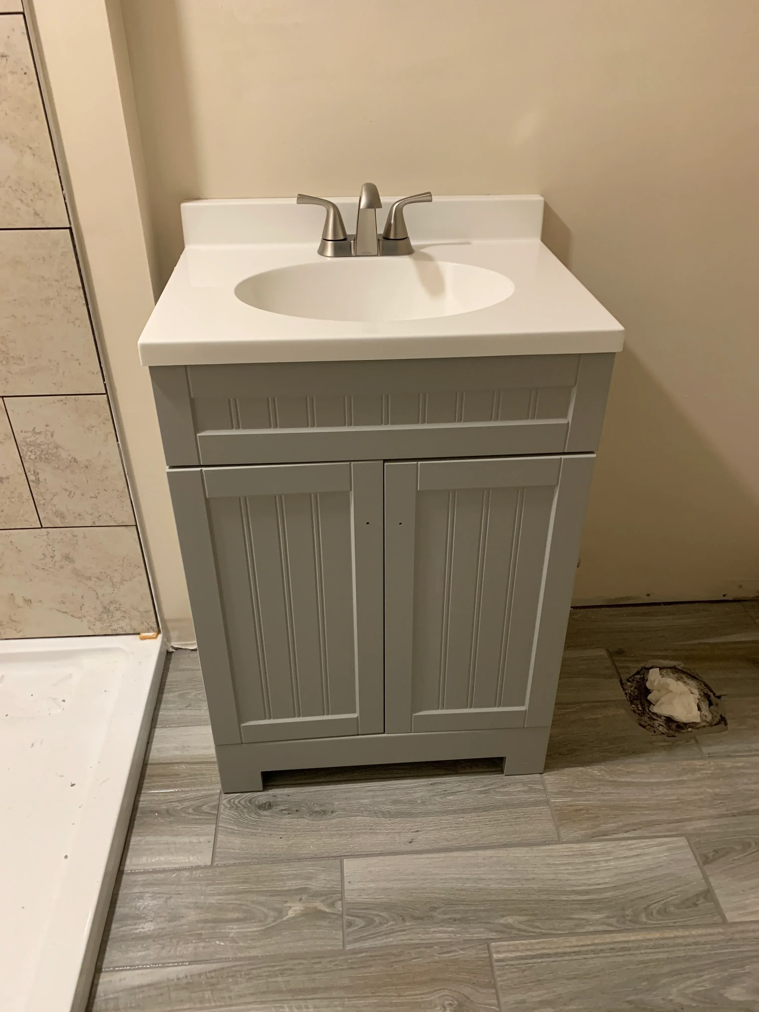 Gray shaker vanity with white sink and brushed nickel faucet, wood-look tile flooring