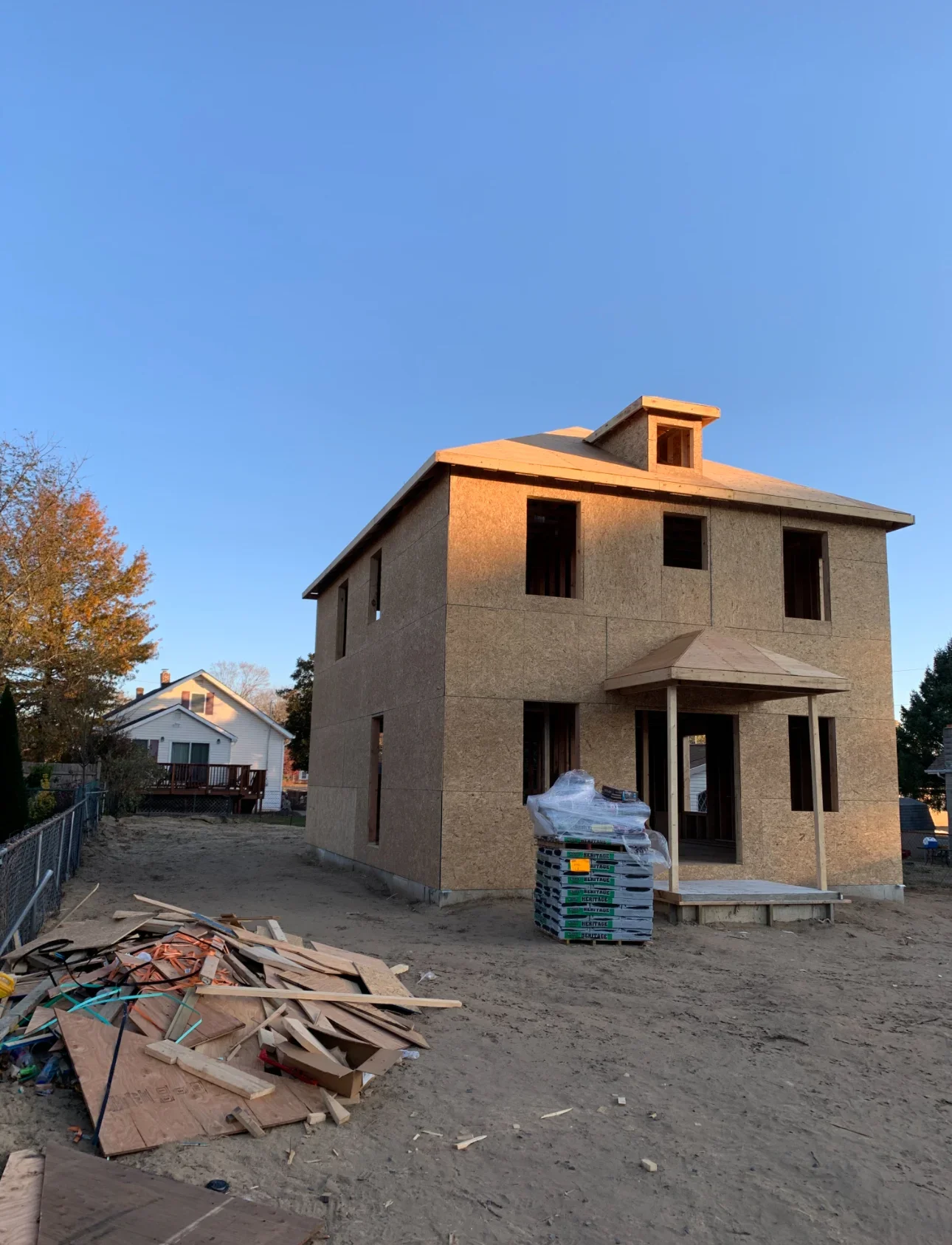Two-story house frame with composite board sheathing, pitched roof, and front porch under construction