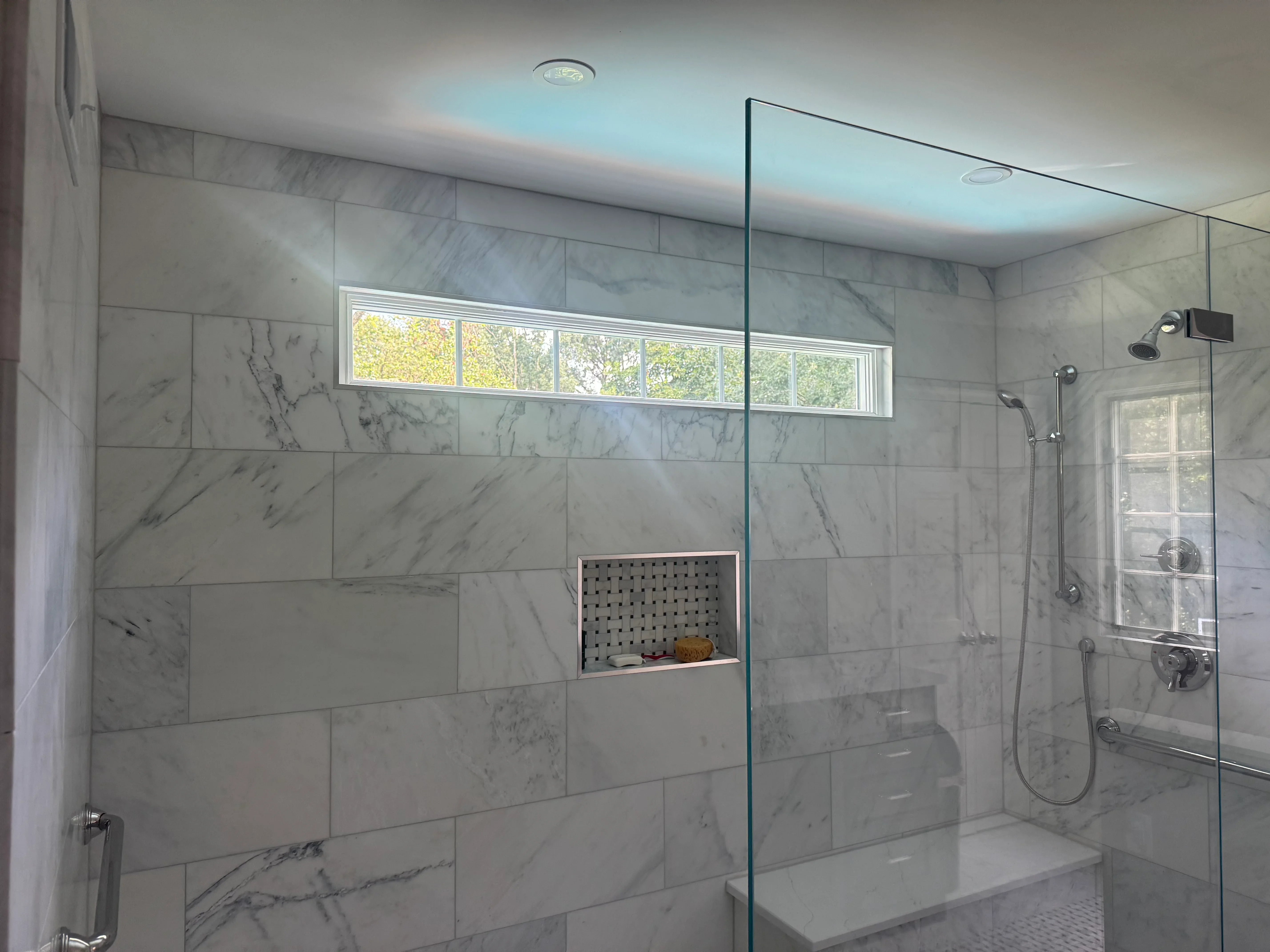 Marble tile shower with frameless glass door, built-in niche, and chrome fixtures