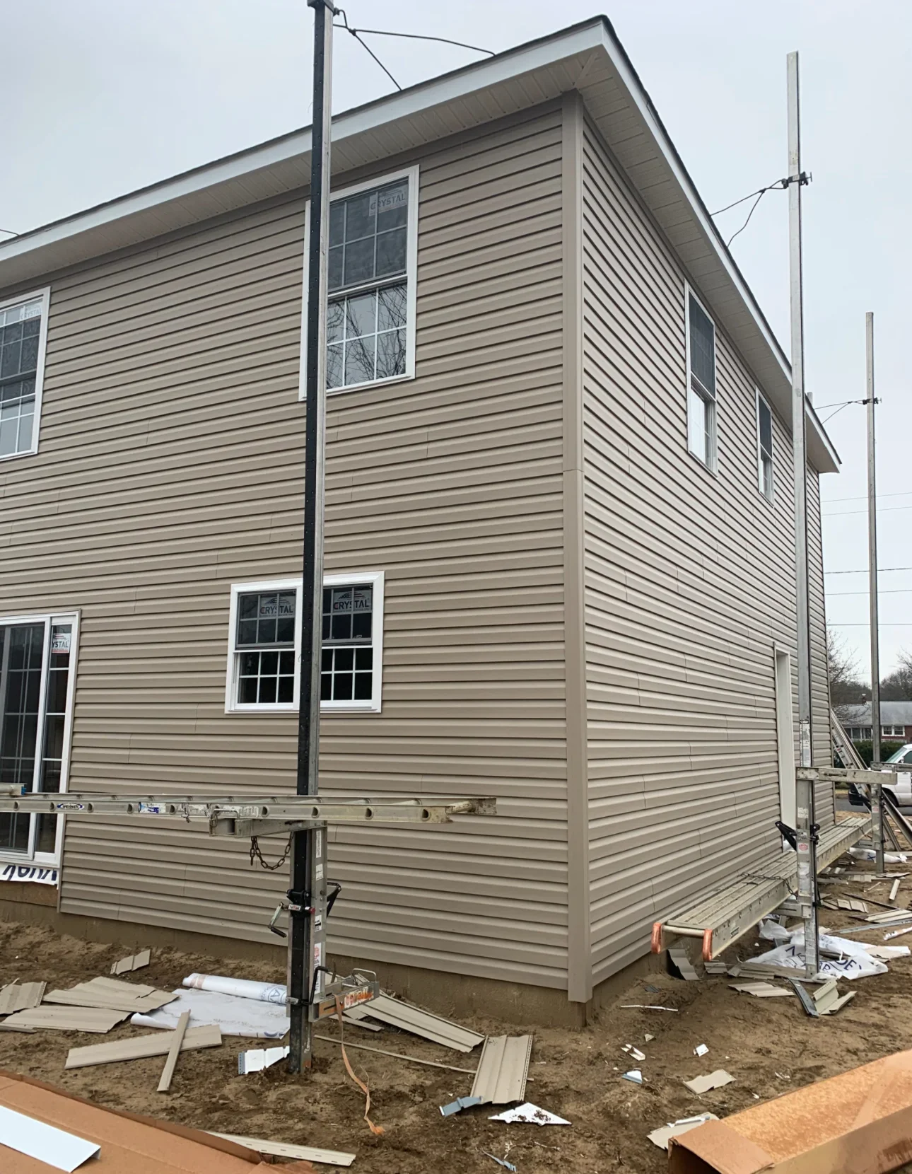 Two-story home with tan horizontal vinyl siding, white-trimmed windows, and metal corner details during installation
