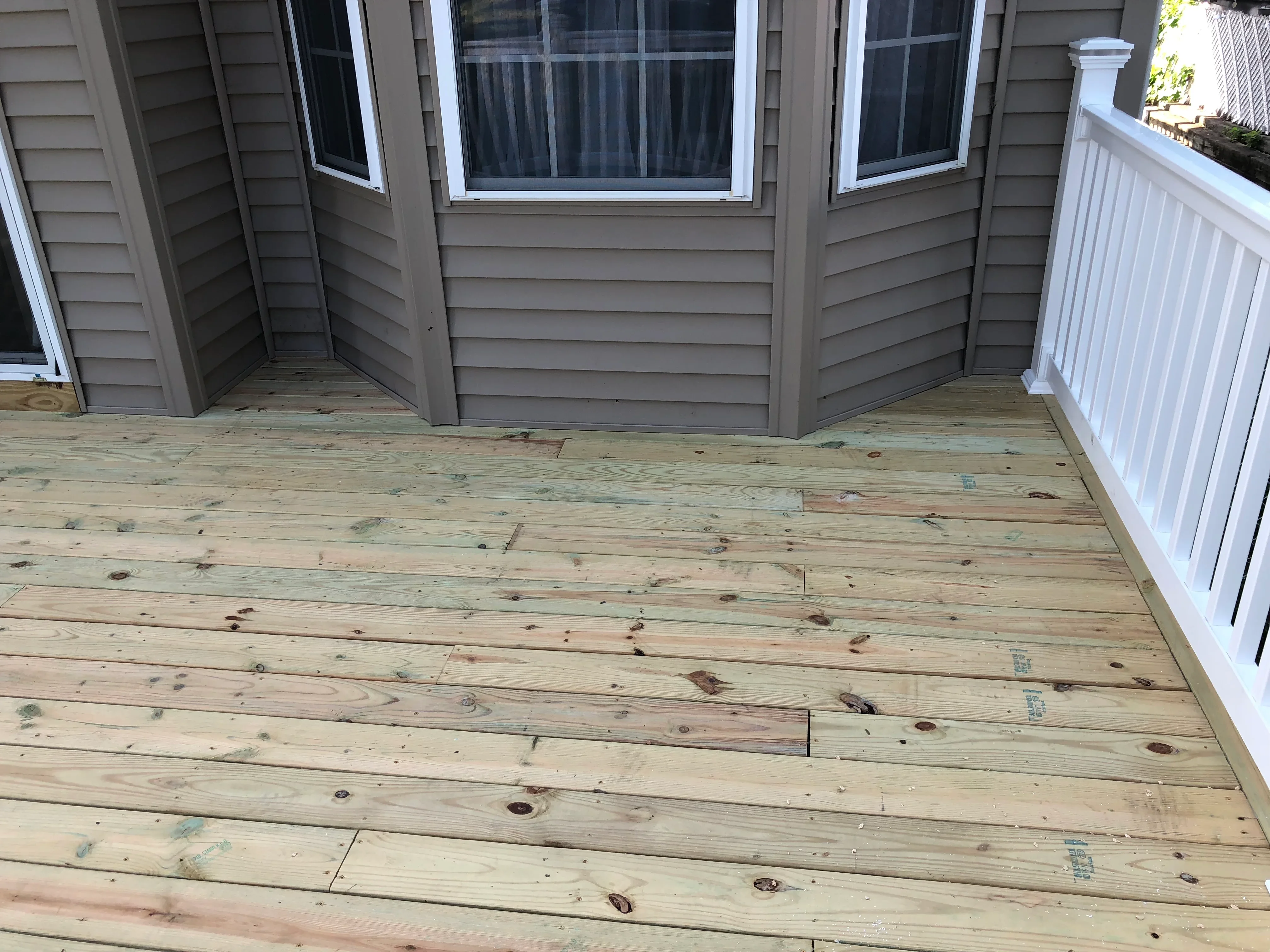 Newly framed pressure-treated wood deck with white vinyl railings and window wells