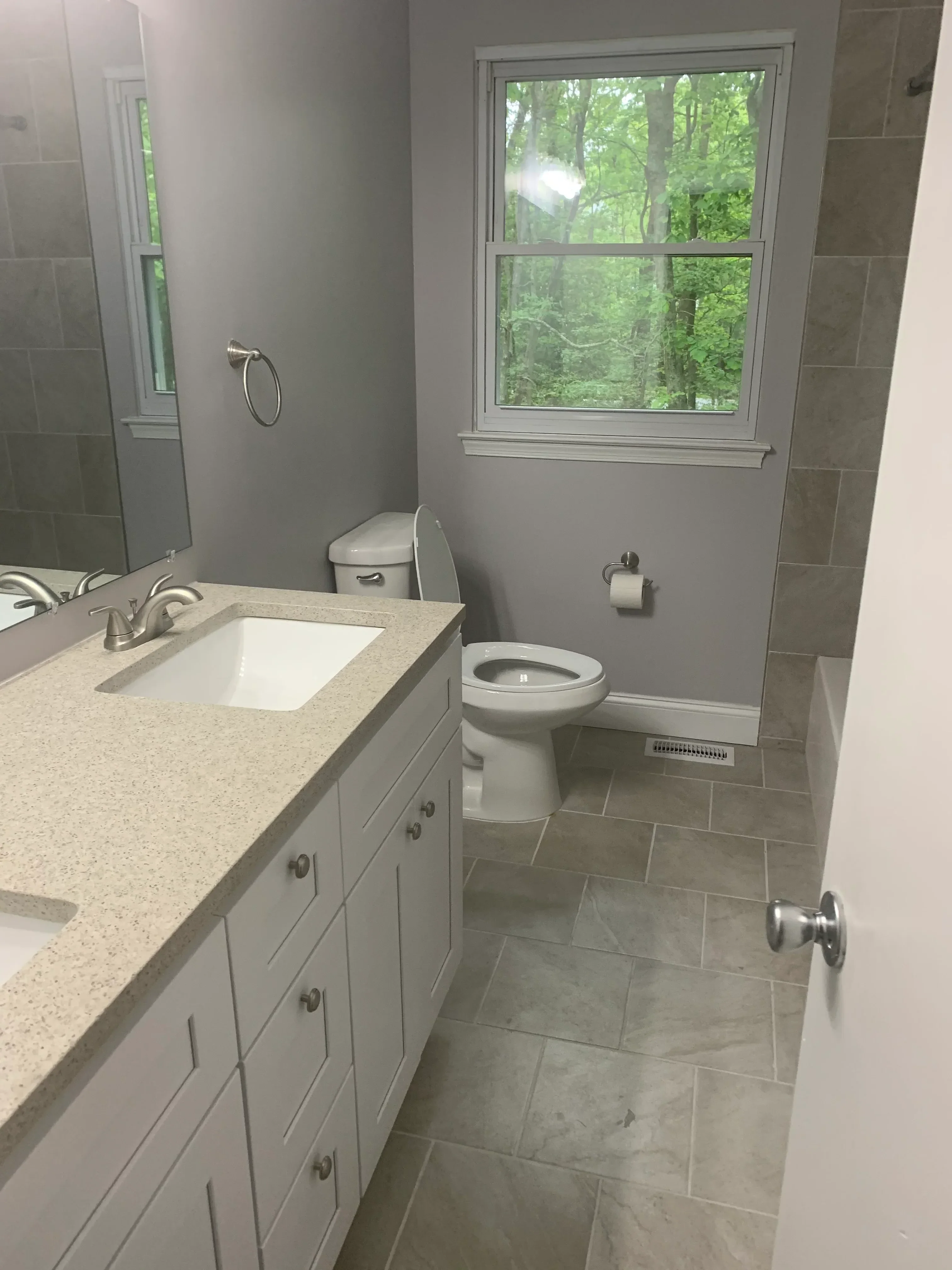Gray tile walls, quartz countertop, white cabinetry, and modern fixtures in renovated bathroom