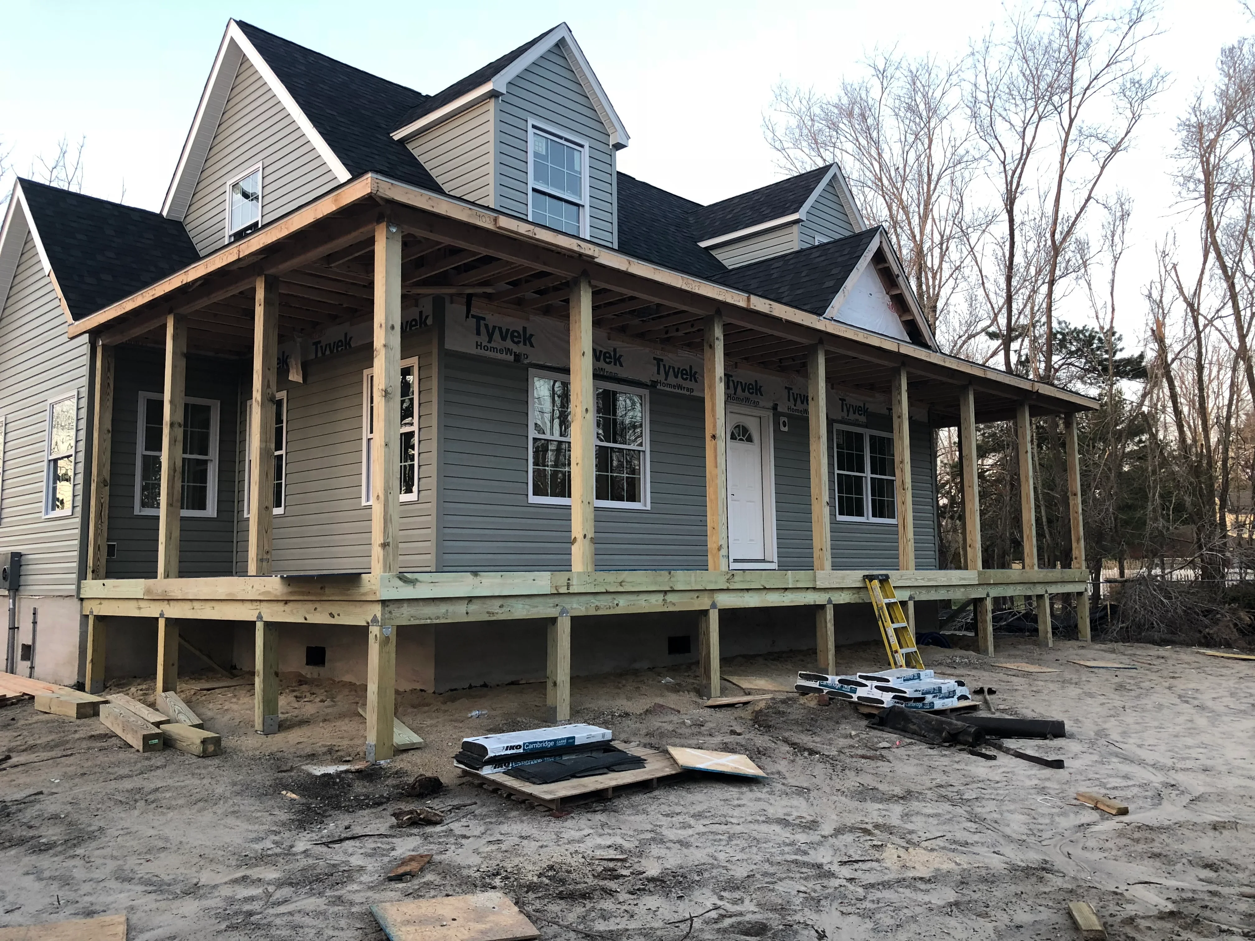 Two-story home under construction with wooden post foundation, fiber cement siding, and gable roof framing