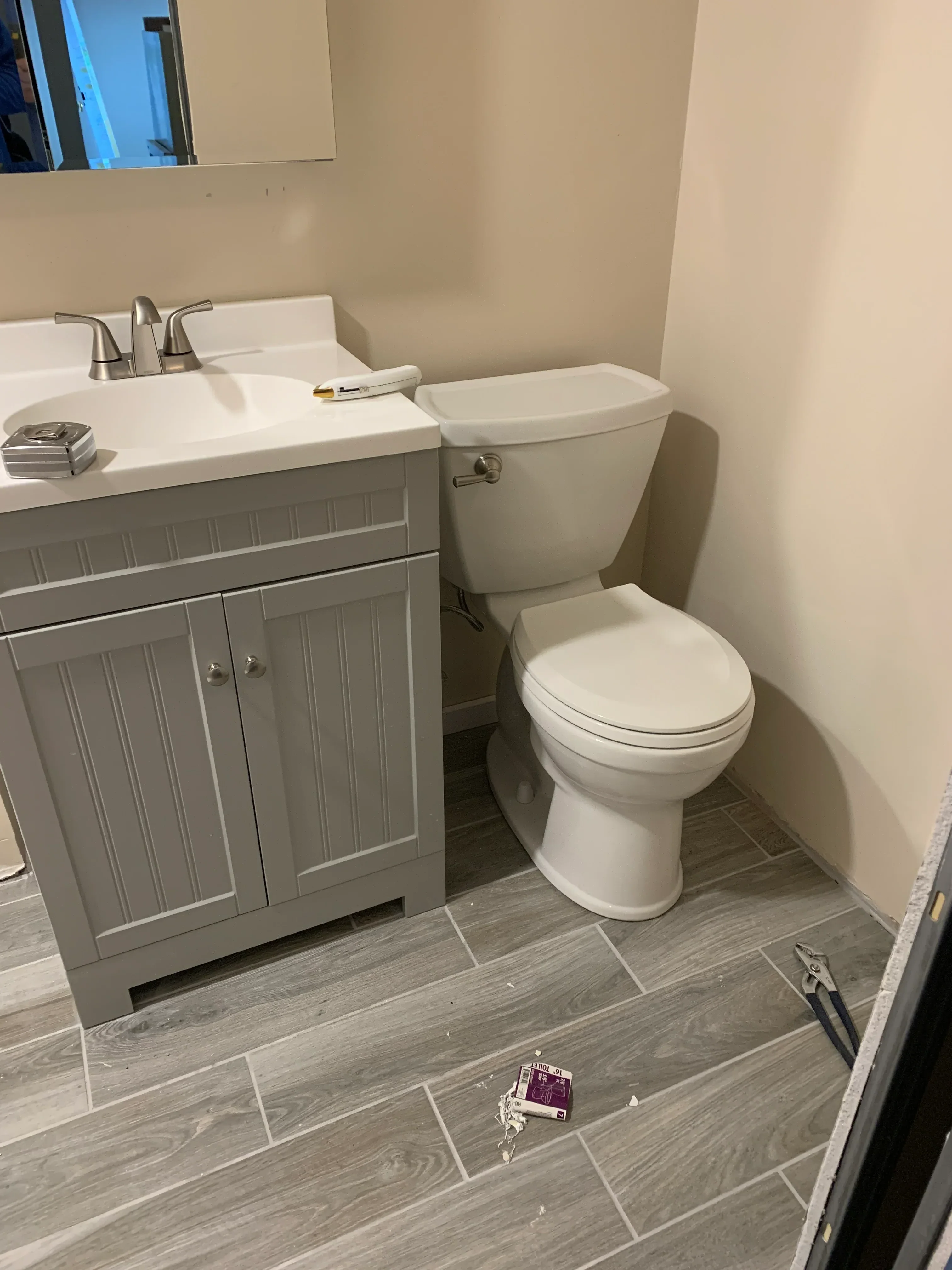 Gray wood-look tile flooring, white drywall, gray vanity cabinet with chrome fixtures in bathroom