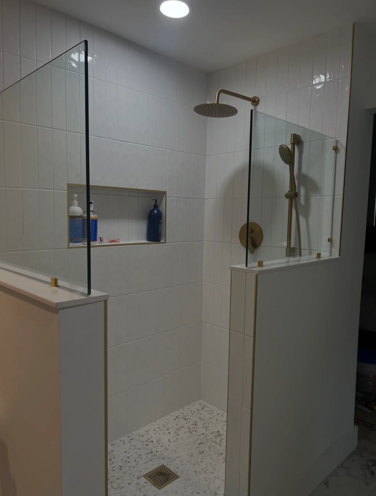 Frameless glass shower enclosure with white subway tile, terrazzo floor, brass fixtures, and built-in niche