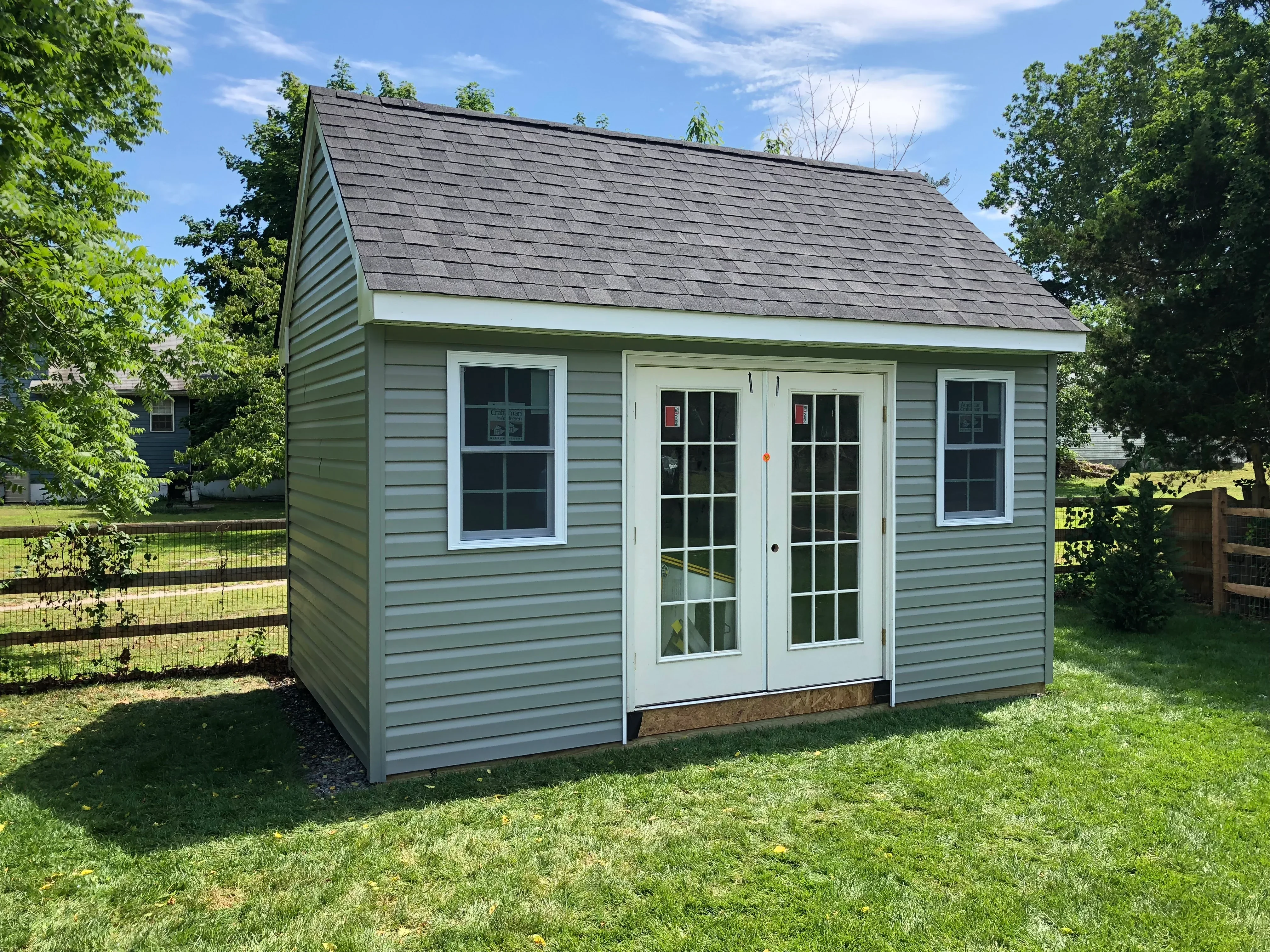 Sage green vinyl siding shed with white trim, architectural shingle roof, and French doors