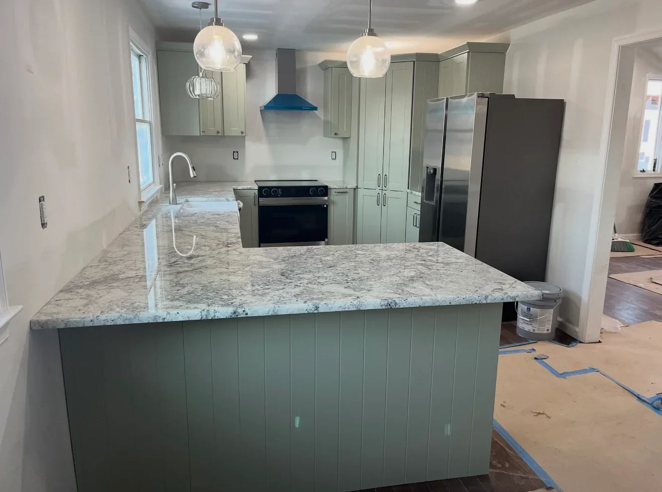 Kitchen with sage green cabinets, granite countertops, stainless steel appliances, and pendant lights