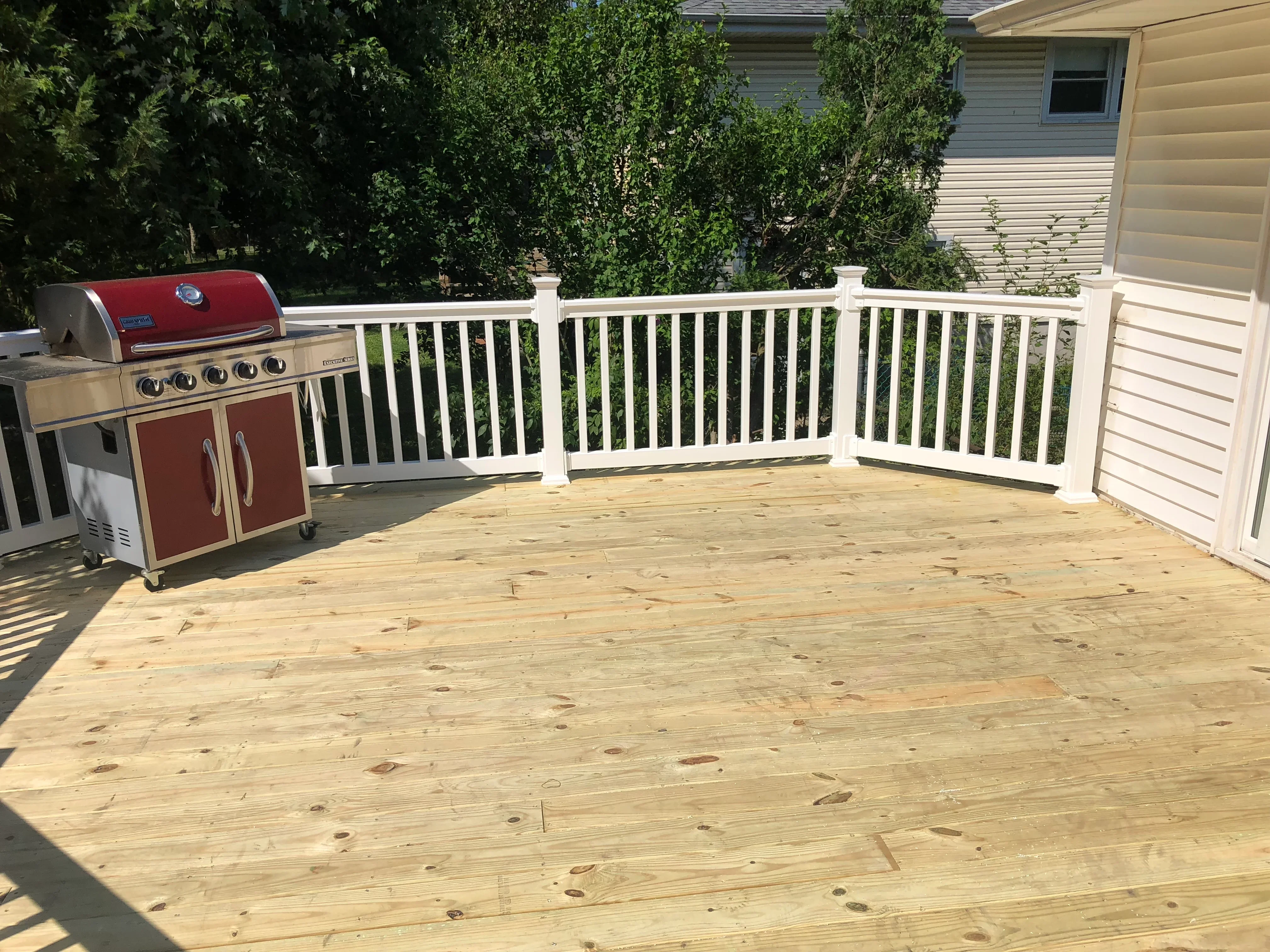 Pressure-treated wood deck with white vinyl railing, built-in grill, and mature landscaping