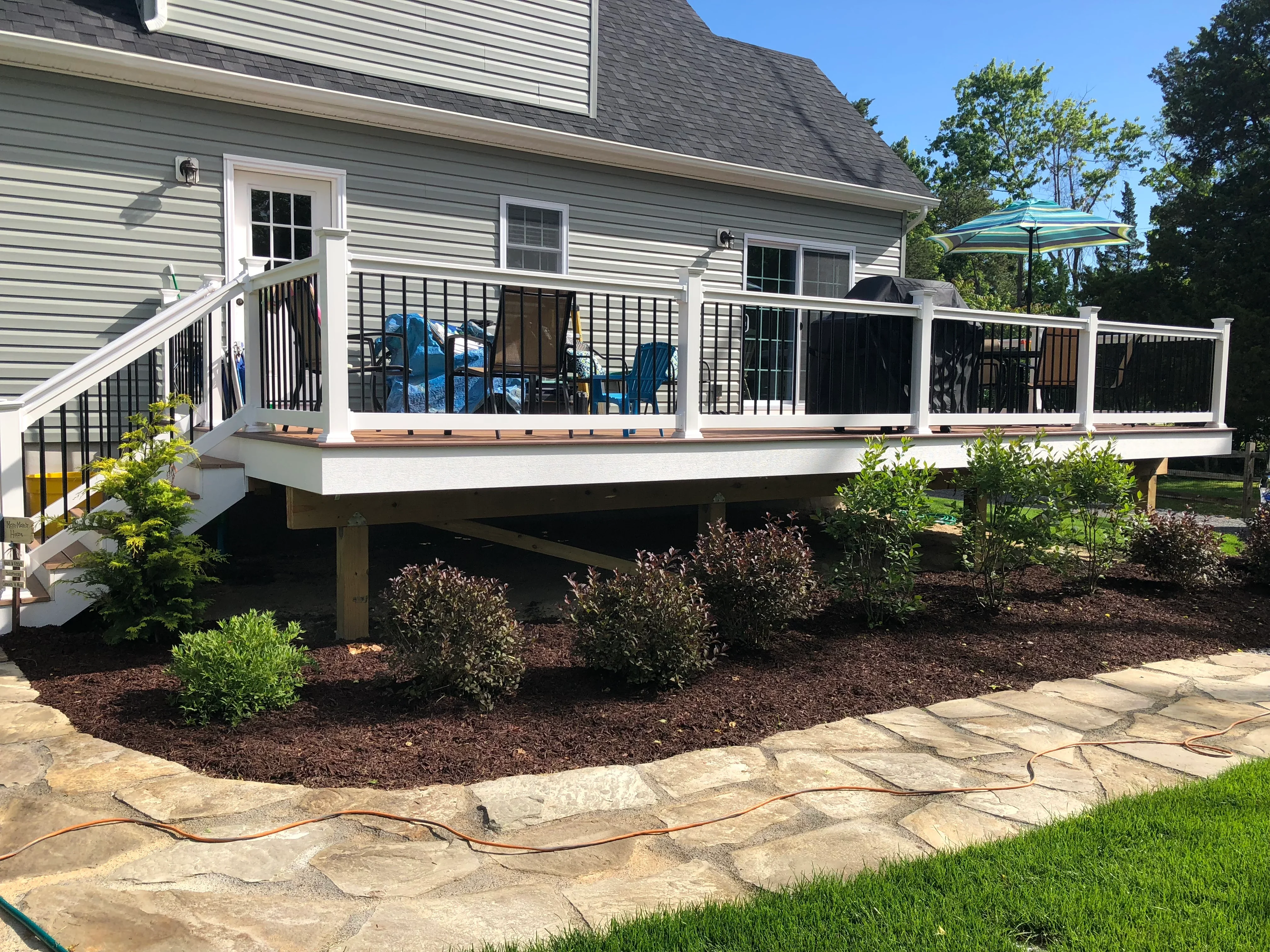 White elevated deck with black metal railing, composite decking, and stone patio below