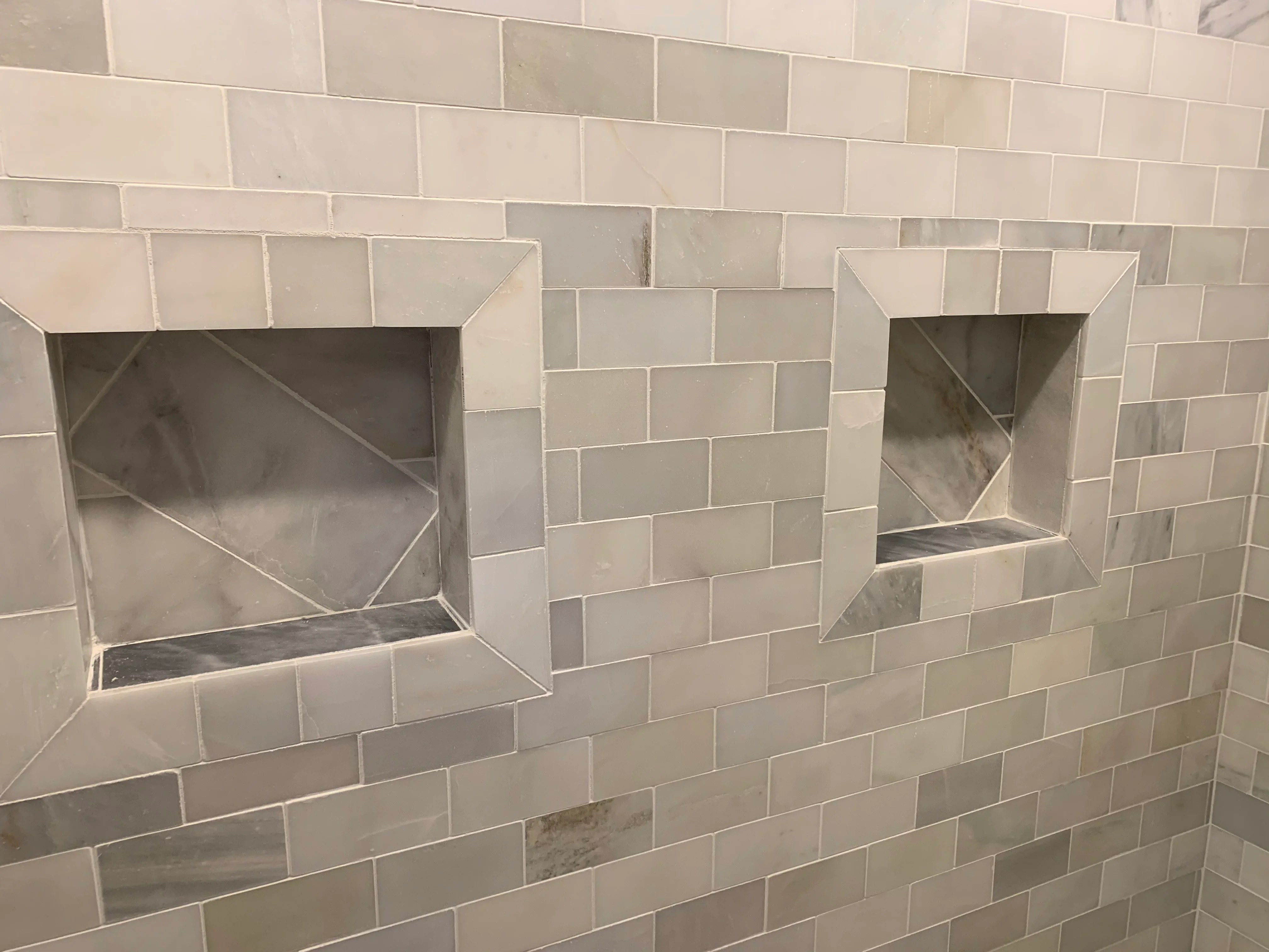 Cream subway tile bathroom wall with two stainless steel recessed niches and diagonal tile detail