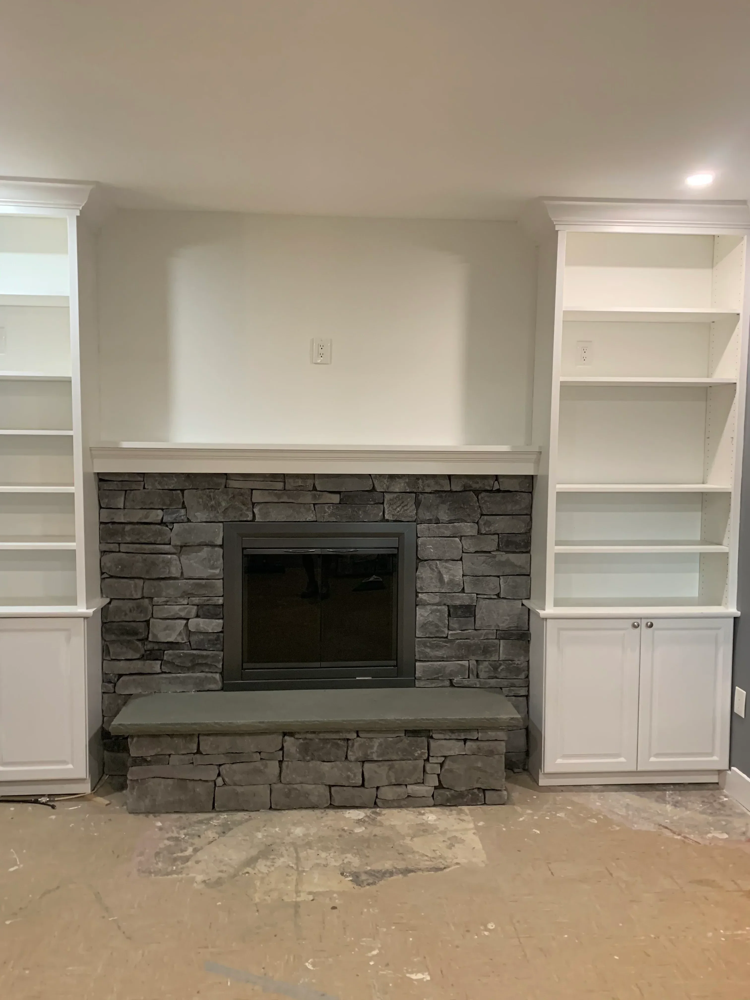 White kitchen cabinets with glass doors and gray stacked stone accent wall with recessed window opening