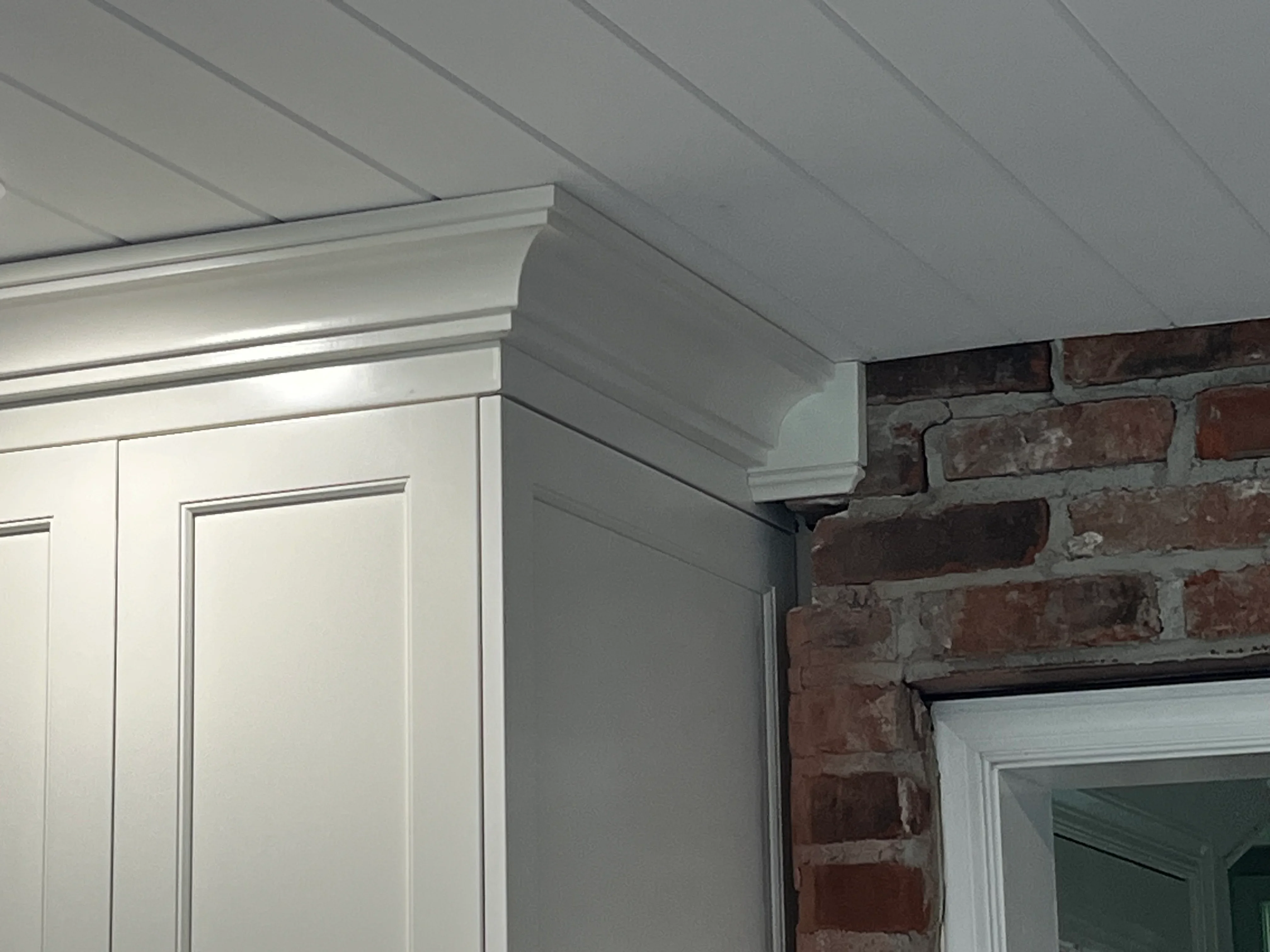 Finished drywall ceiling with crown molding trim and soffit framing around brick chimney