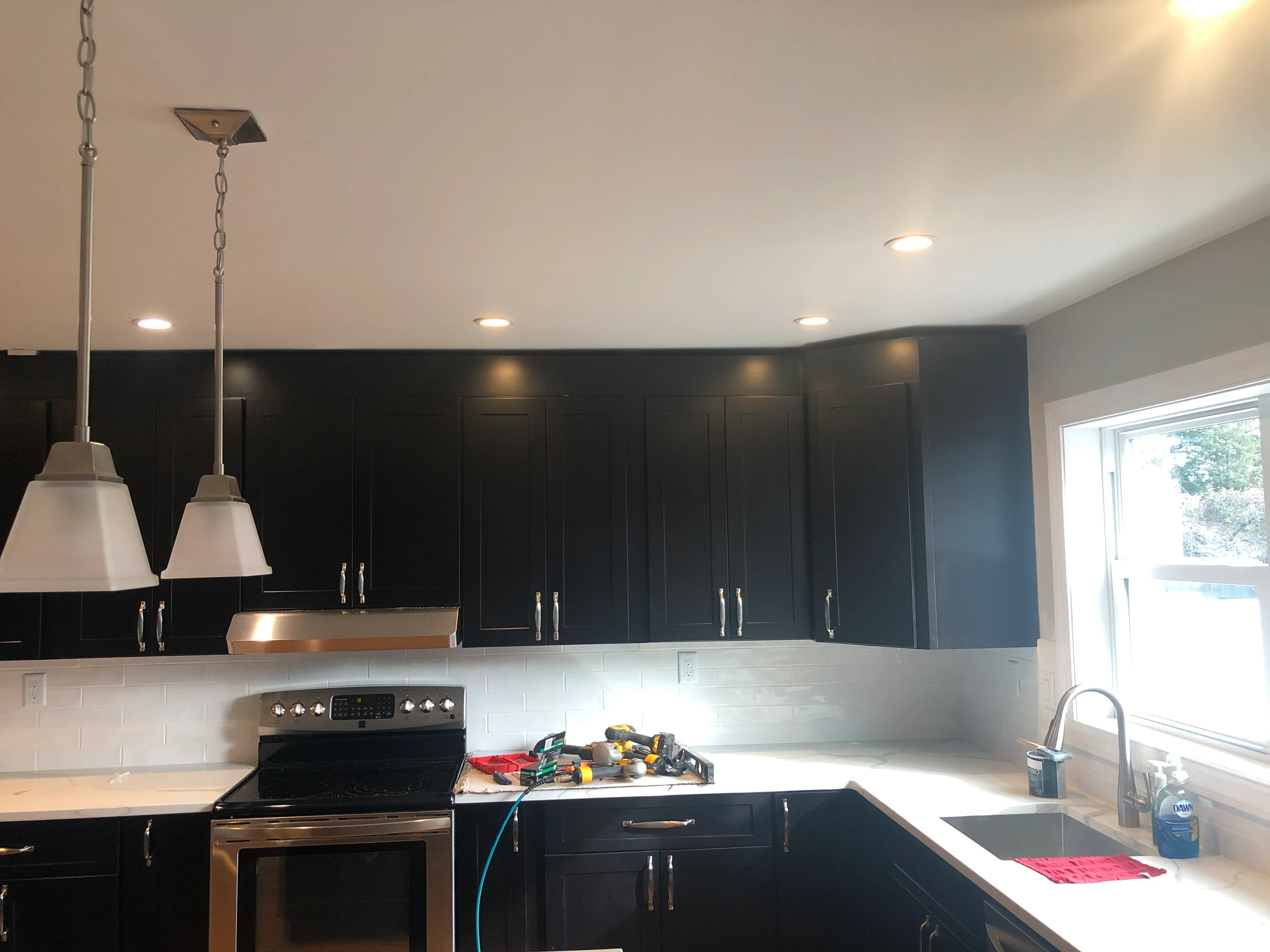 Black cabinetry, white subway tile backsplash, recessed lighting, and stainless steel appliances in modern kitchen
