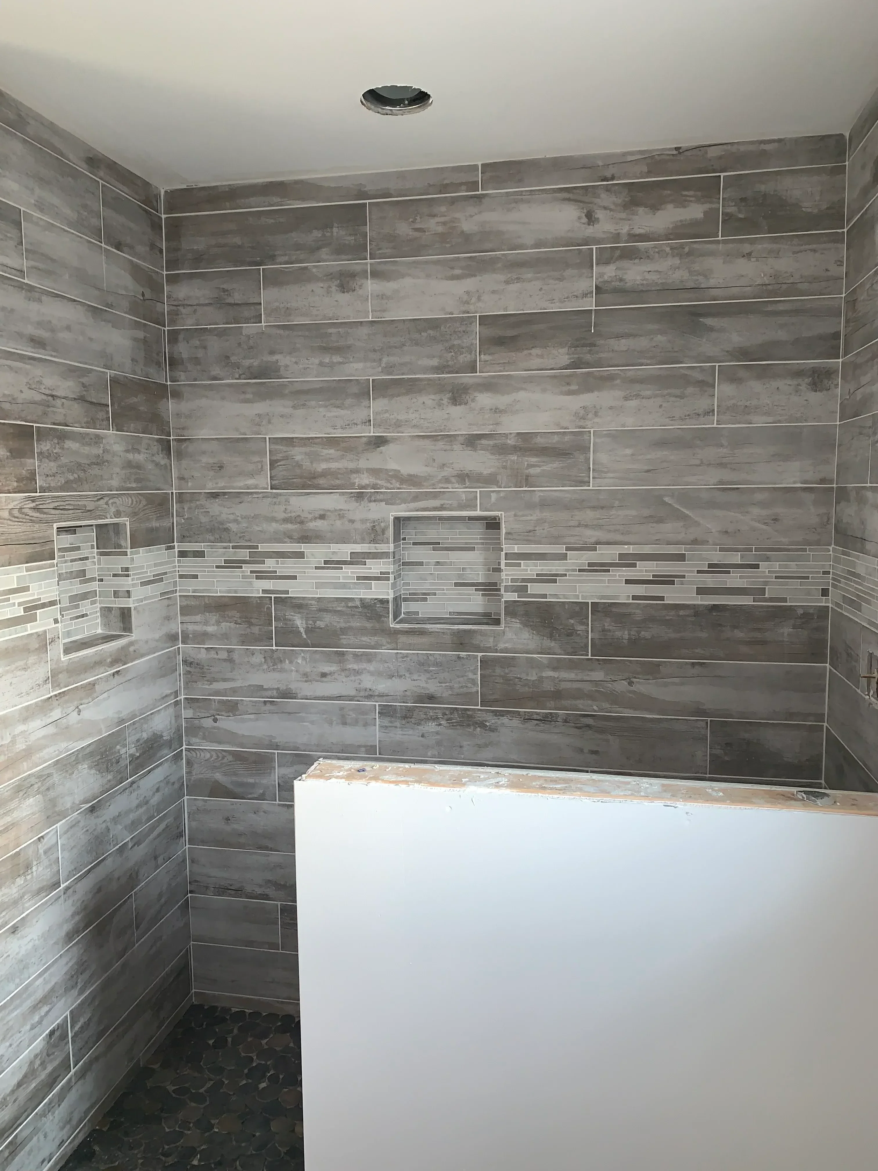 Gray wood-look porcelain tile shower with linear mosaic accent strip and recessed niche