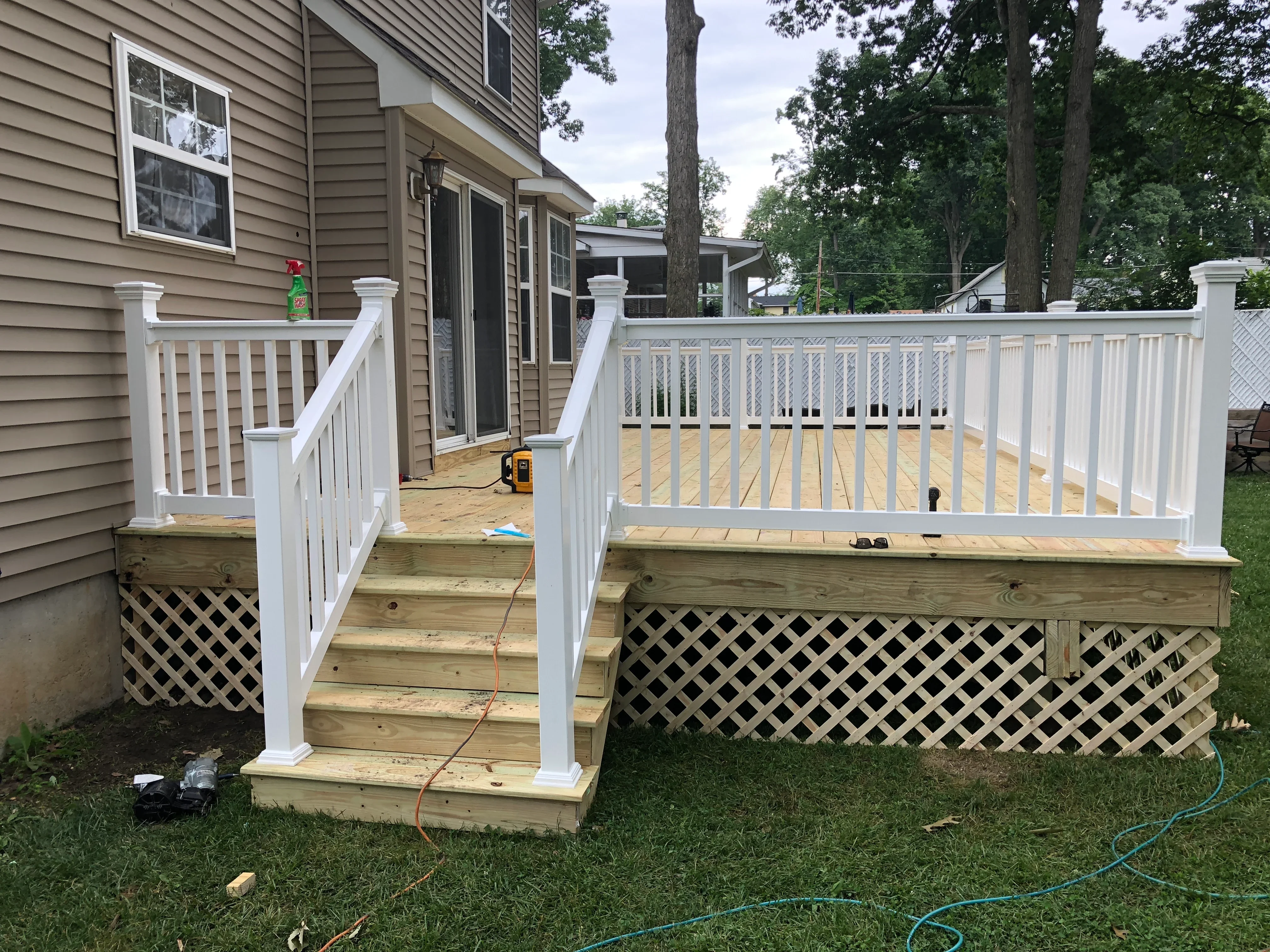 Elevated wooden deck with white vinyl railings, lattice skirting, and pressure-treated lumber framing