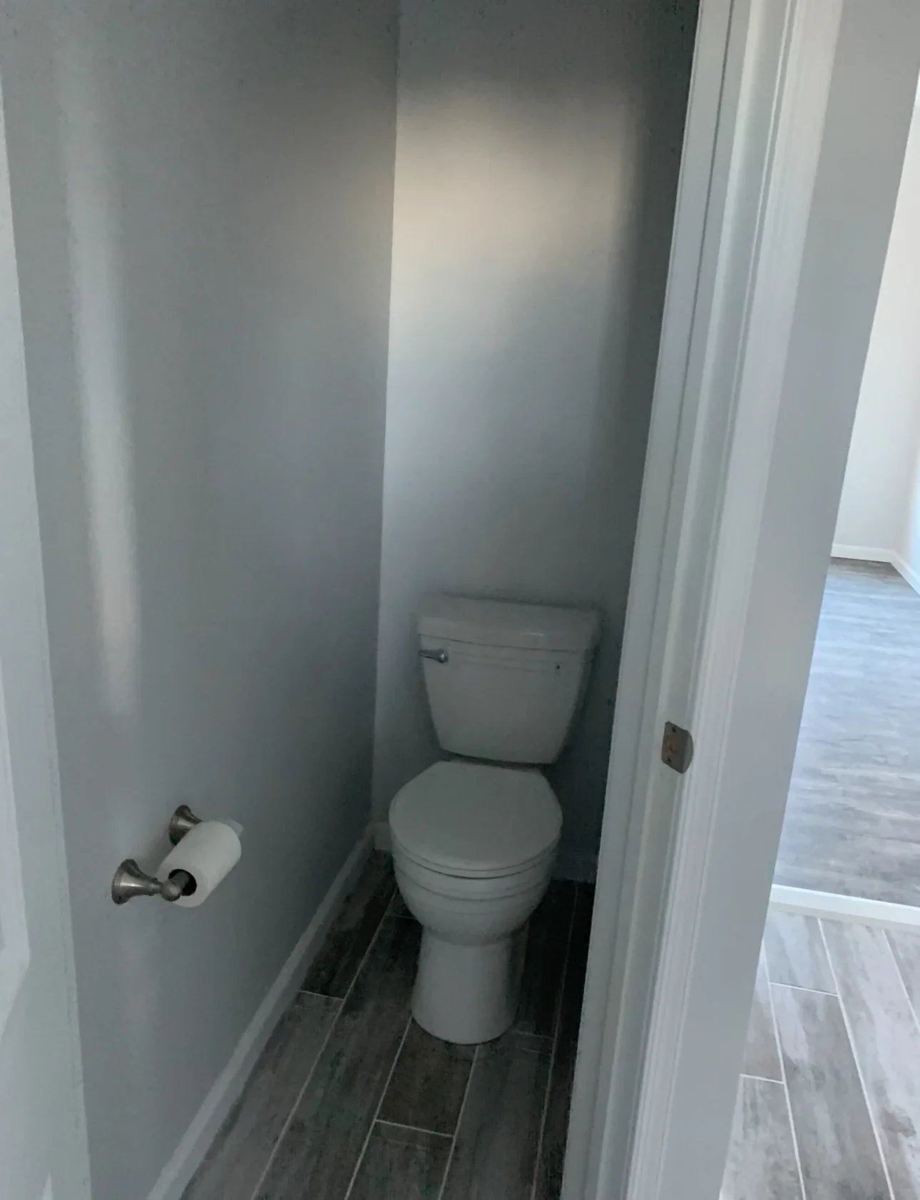 Newly renovated half bath with gray drywall, dark wood-look tile flooring, and white toilet
