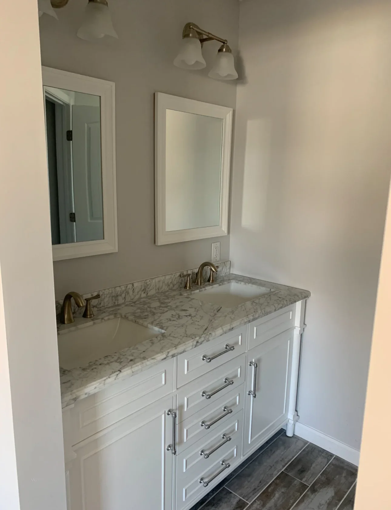 White bathroom vanity with marble countertop, dual mirrors, and dark tile flooring